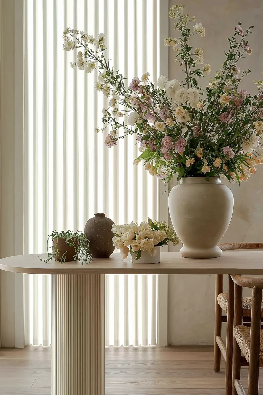 Apartament Lacu Moriil – decor minimalist pe o masă din lemn cu trei plante în ghiveci mic și o vază mare cu un aranjament de flori albe și roz, creând un detaliu interior elegant și liniștit.