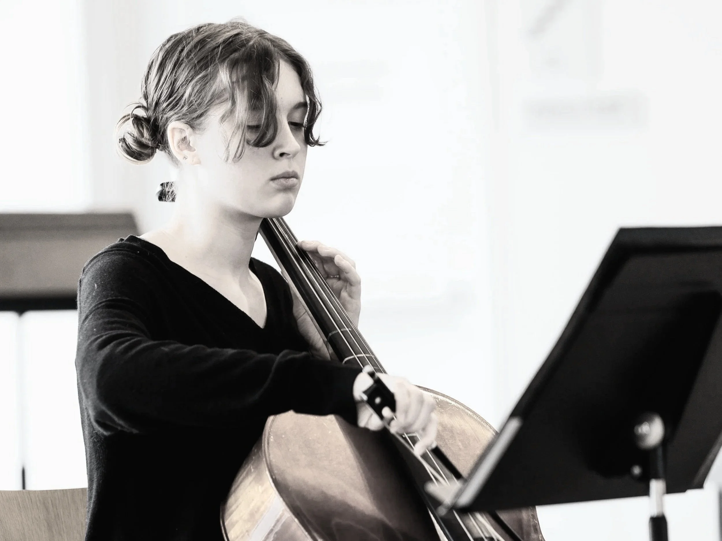 Young girl playing the cello while reading sheet music.