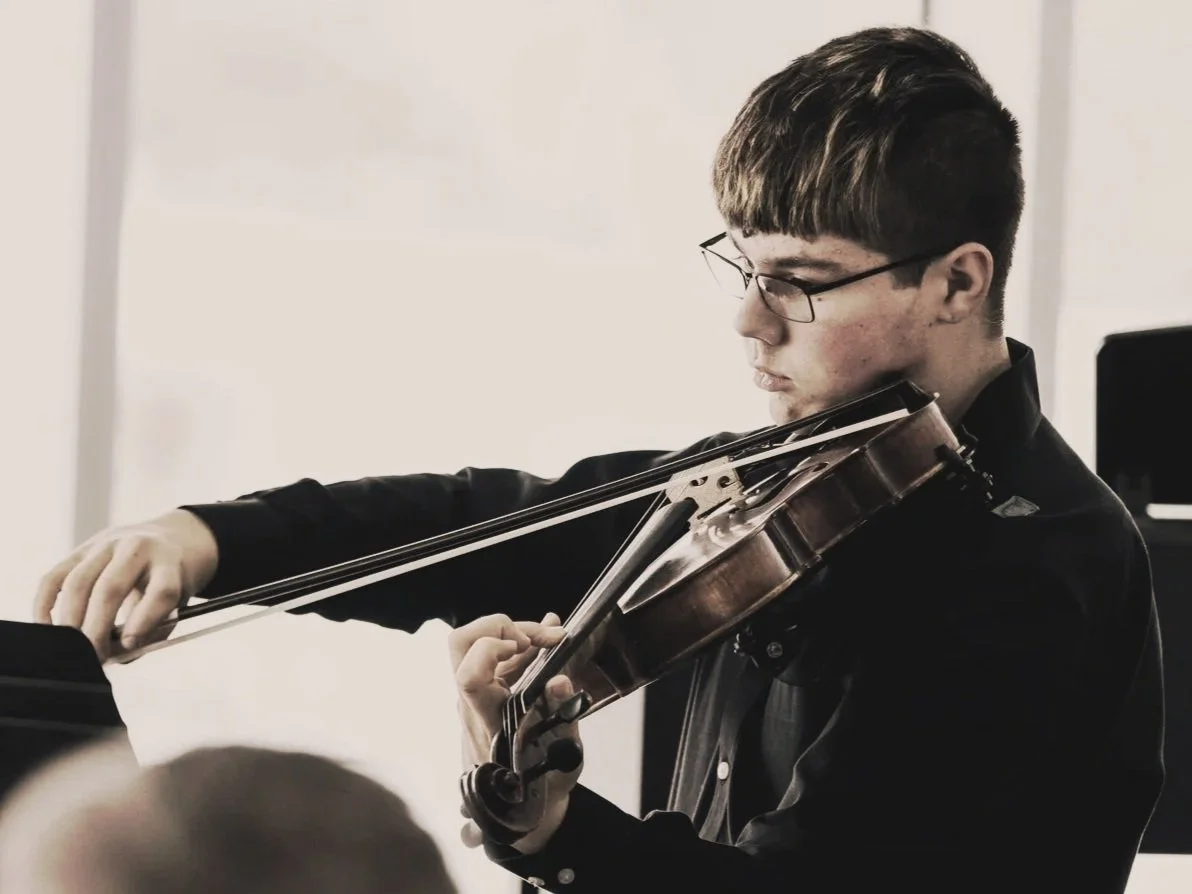Young man wearing glasses playing the viola in a bright room.