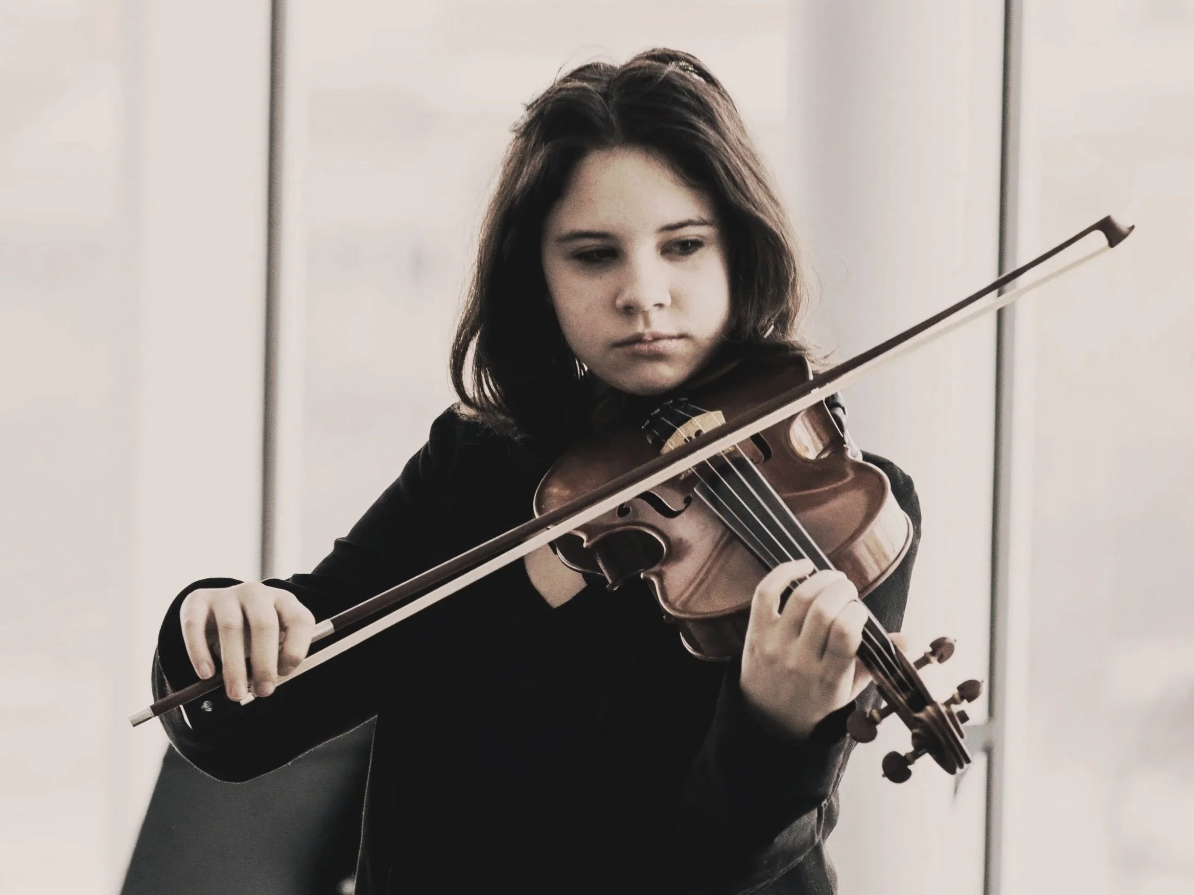 Young girl playing the violin indoors, with a serious expression.
