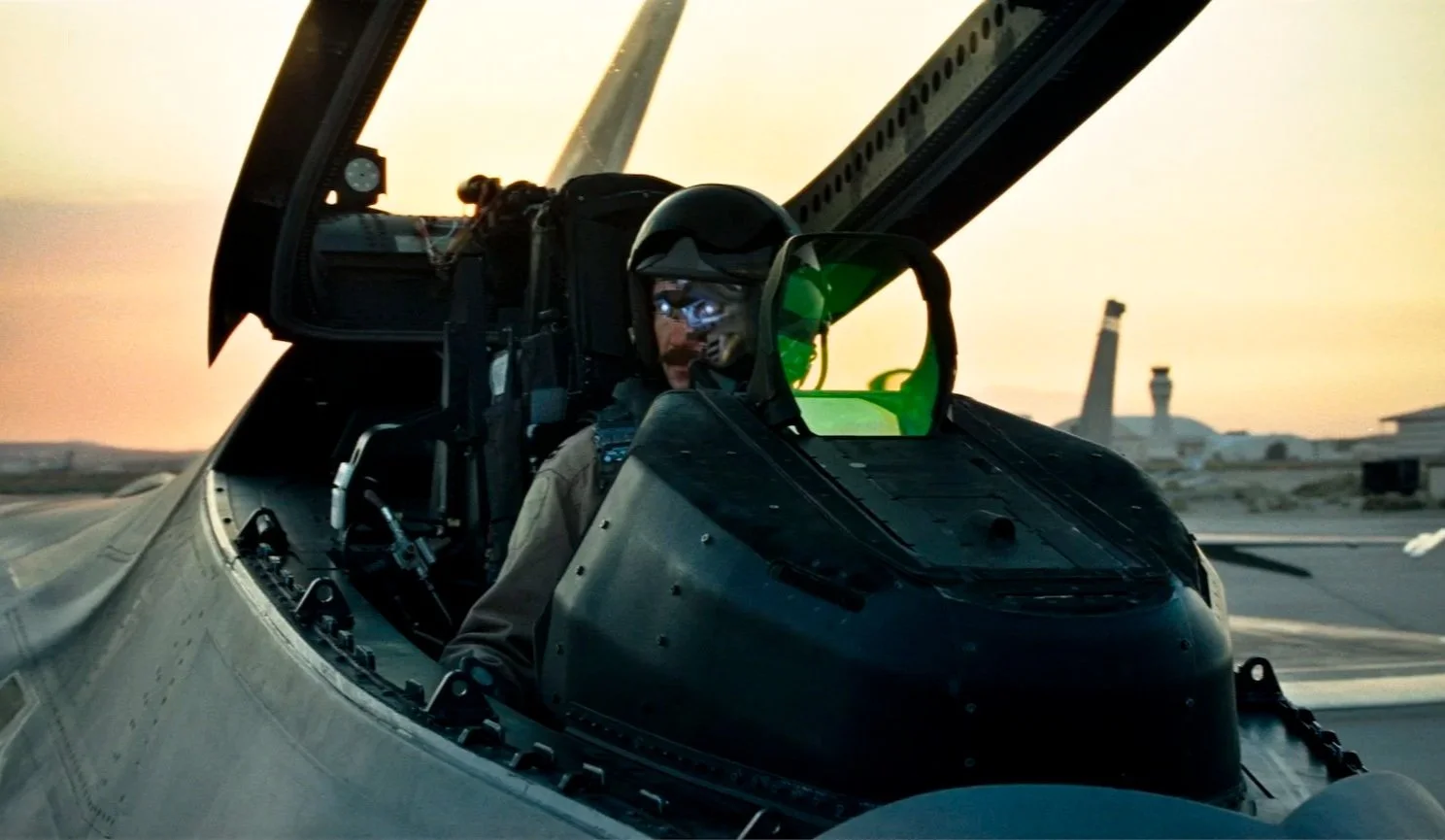 Brian Reece sitting in the cockpit of a fighter jet with a sunset in the background. Moustache Man in Starscream from Transformers.