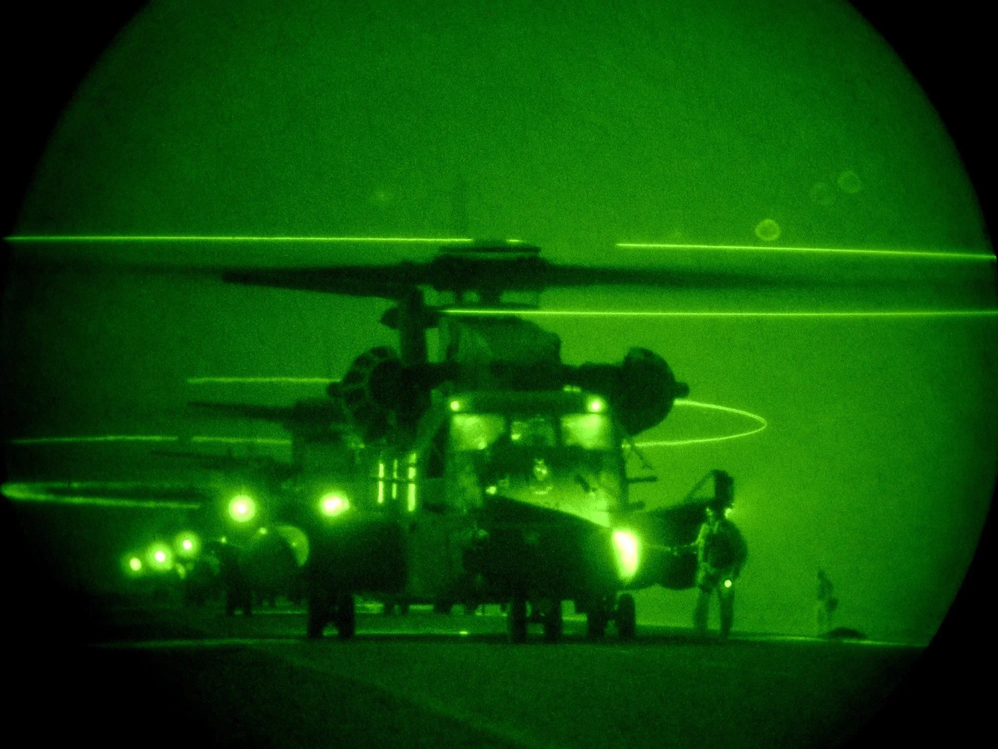 Night vision photo of a MH-53 helicopters at night, with crew members nearby.