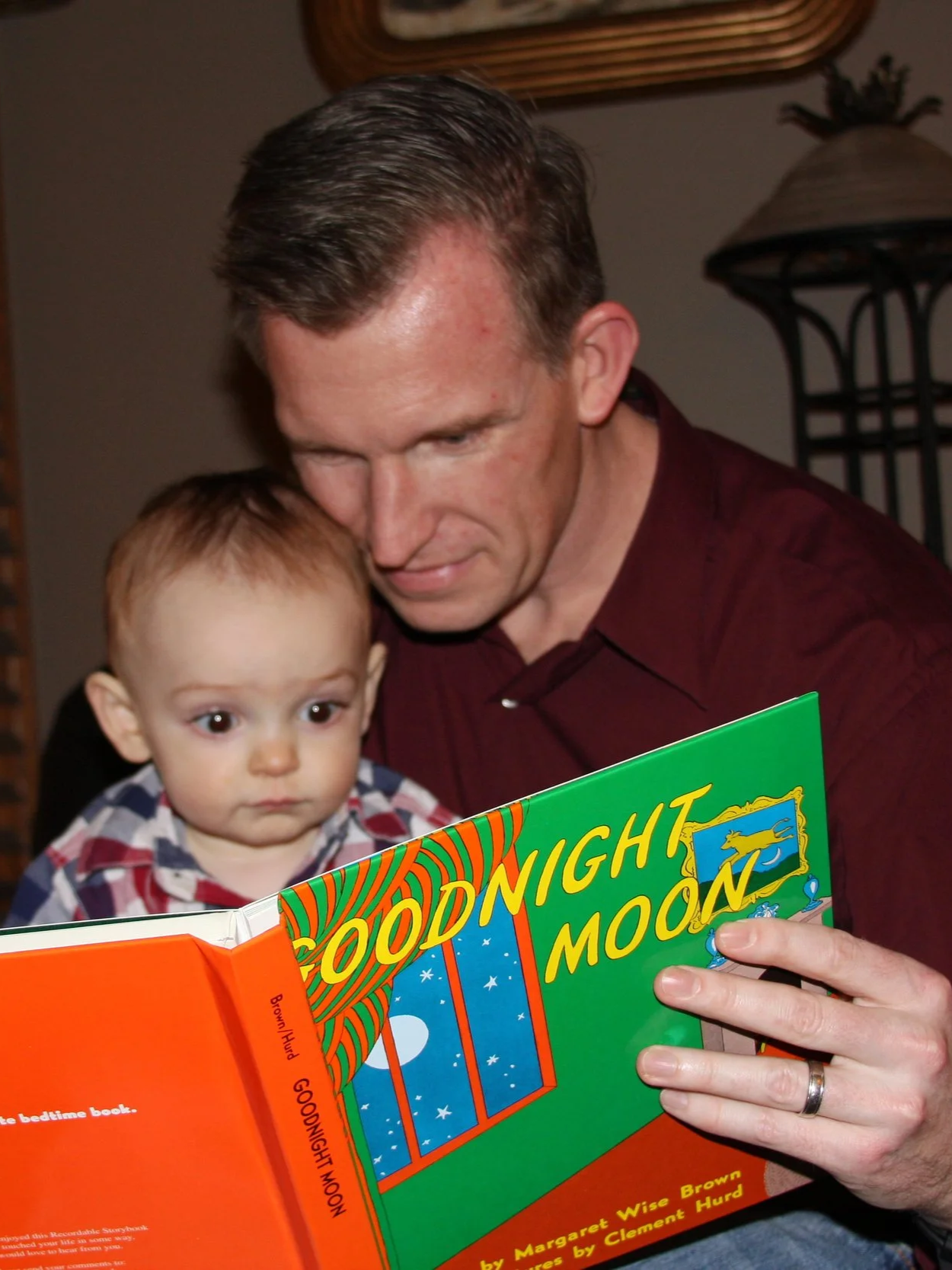 Brian Reece reads a children's book titled 'Goodnight Moon' to a young child, both looking at the book.