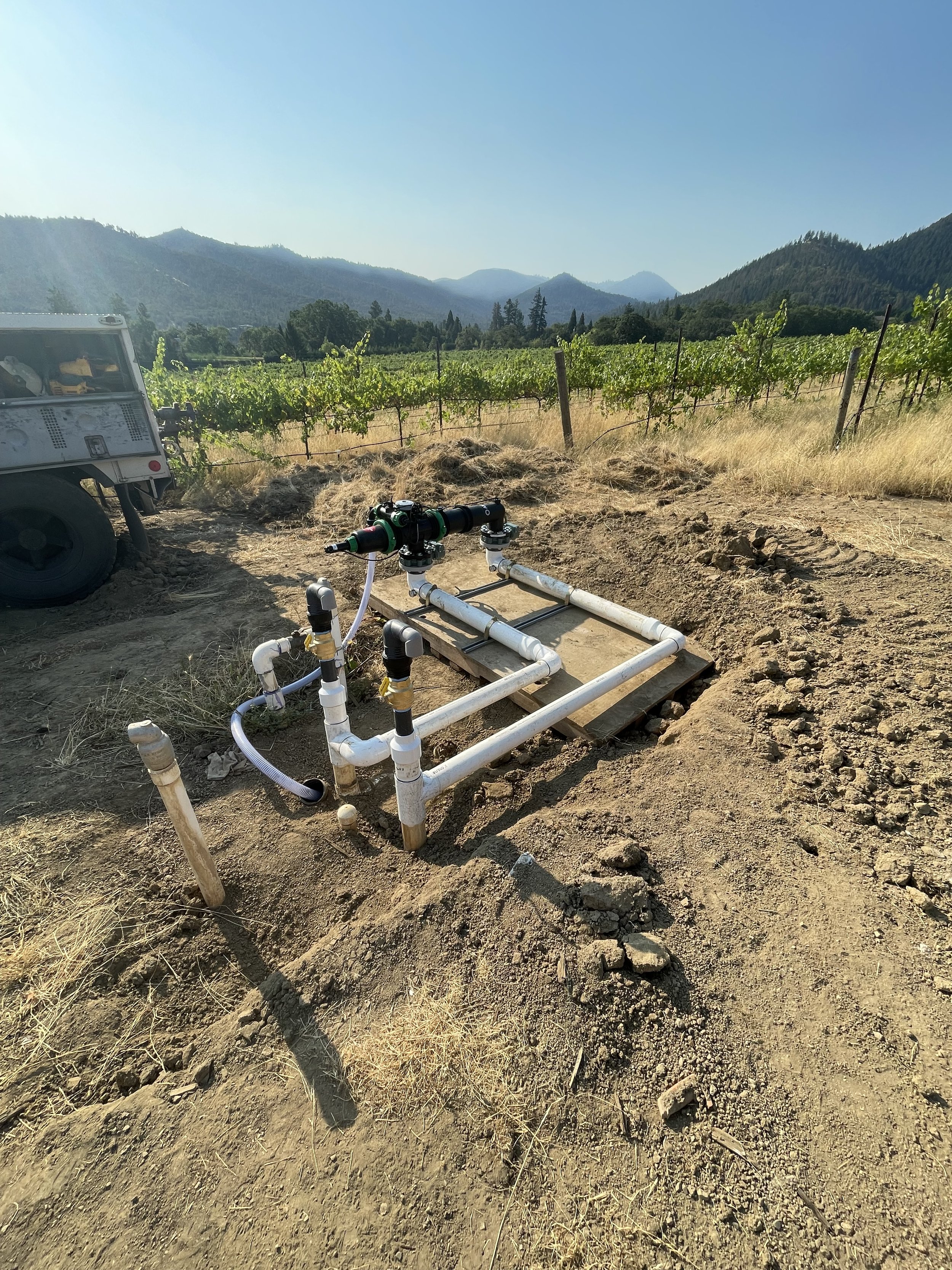 Irrigation filtration system with pipes and valves set up in a vineyard with mountains in the background.