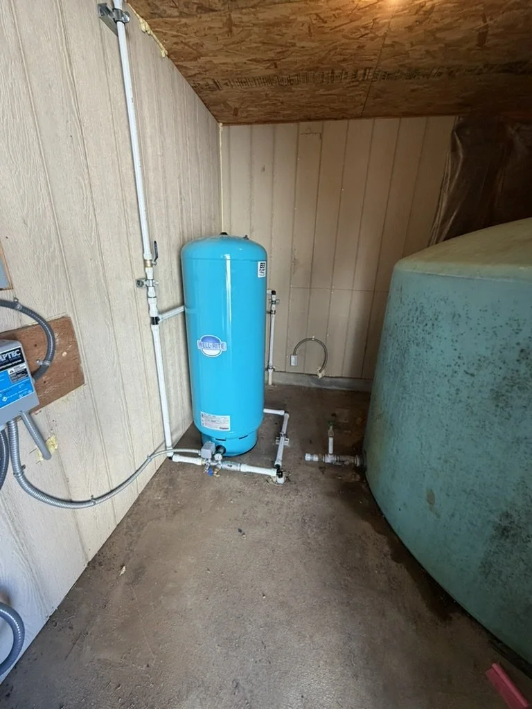 A water pressure tank unit connected to plumbing pipes and an electrical control box inside a utility room with wooden walls and floor in jacksonville