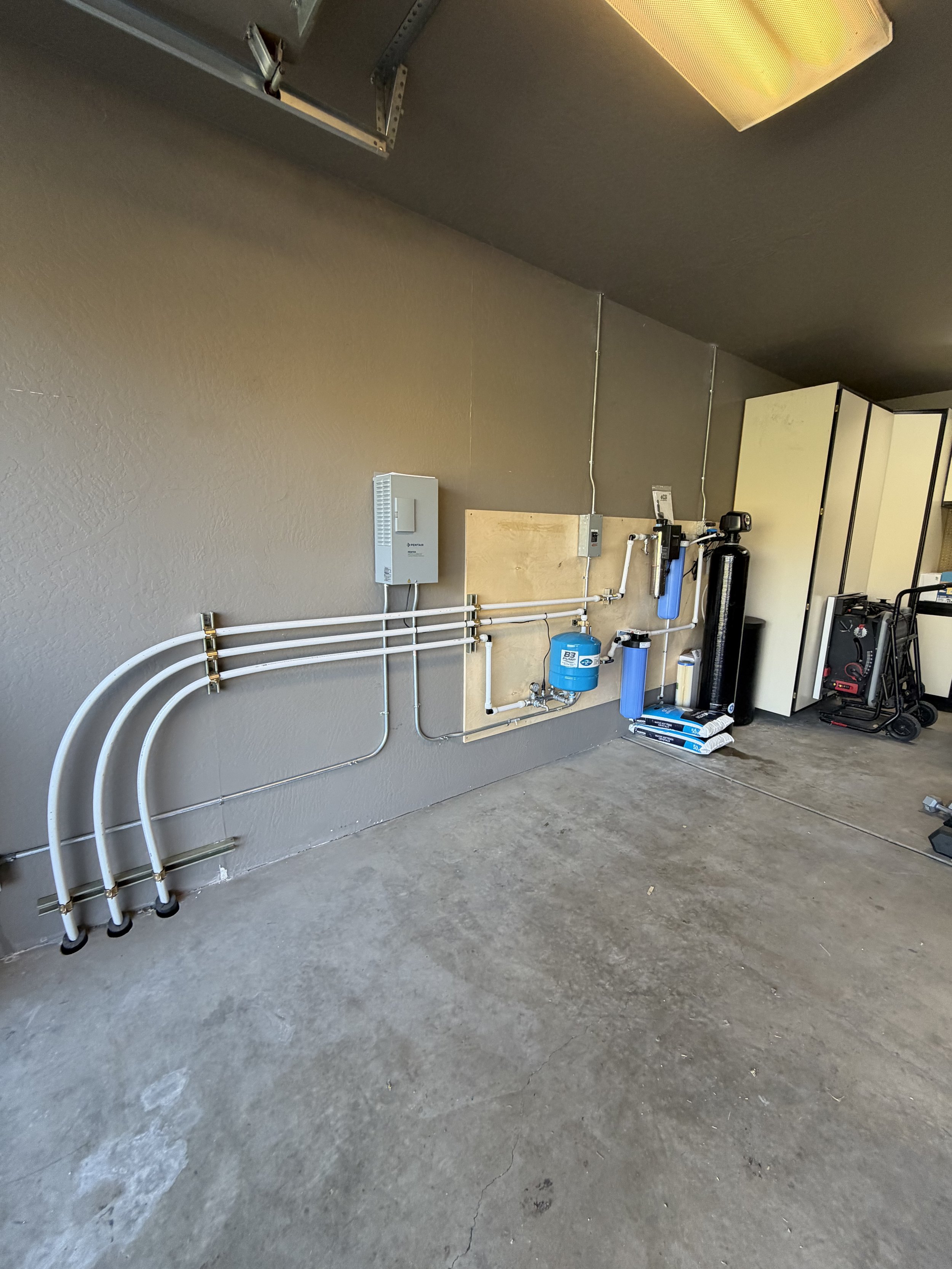 Garage wall with piping, water filtration system, and cabinets. Concrete floor with visible cracks.