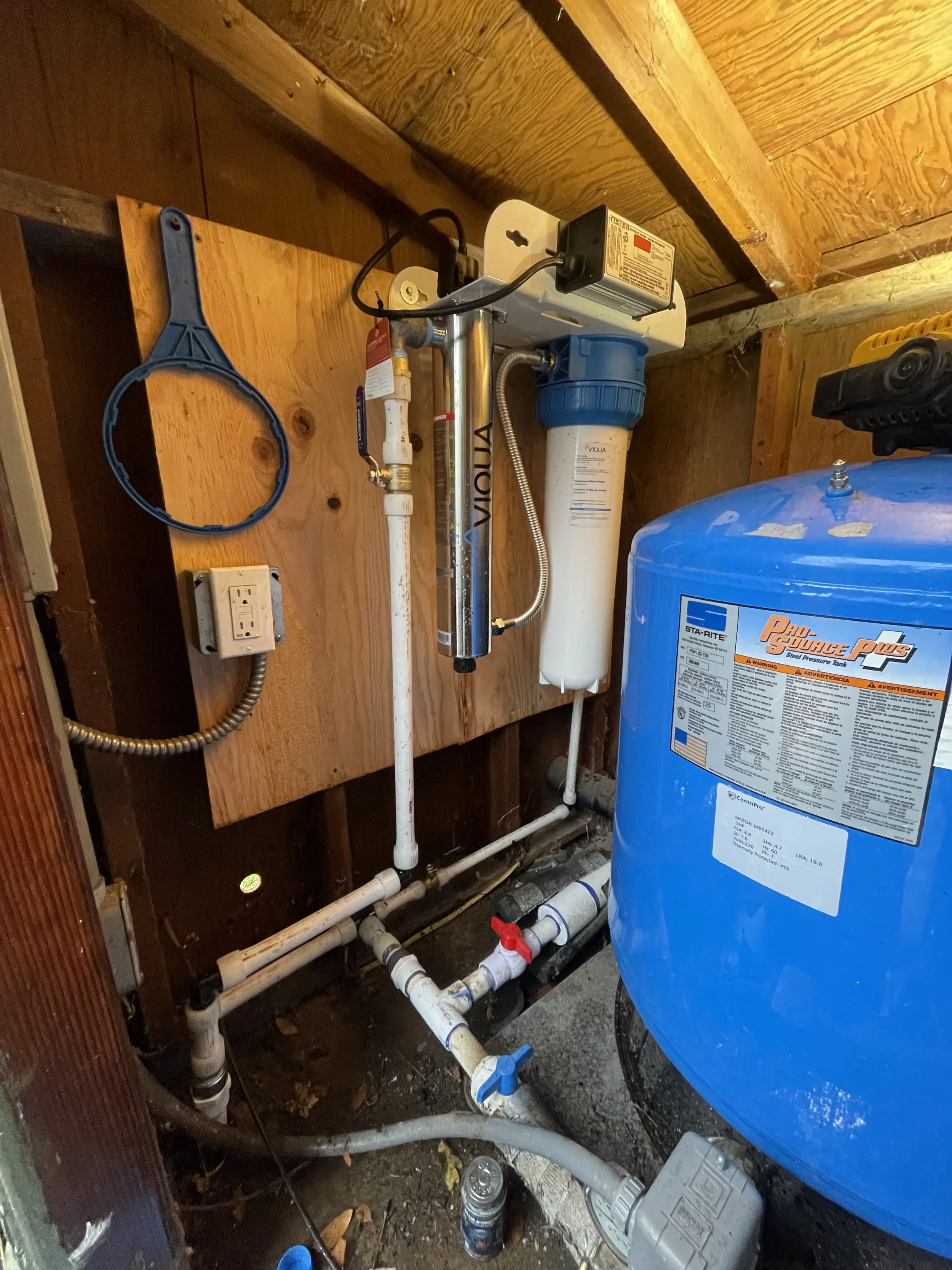 UV Water filtration system with pipes, filters, and a large blue tank in a basement utility area.