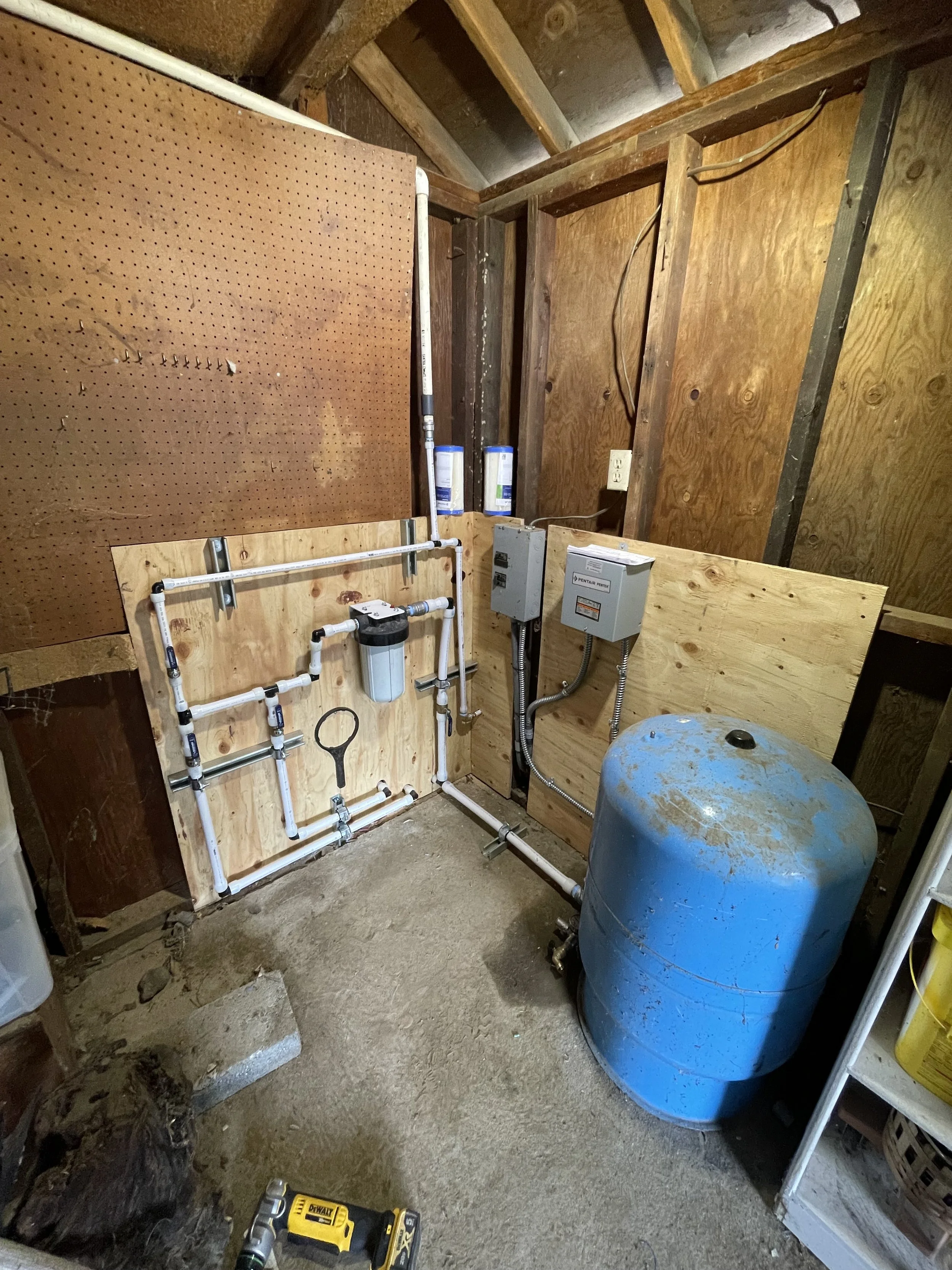well pump room with a blue pressure tank and filtration equiptment in an unfinished basement or utility room.