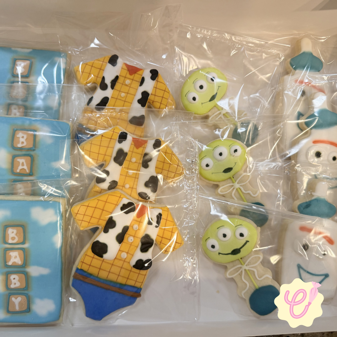 Assorted decorated cookies with Toy Story theme, including cowboy shirts, aliens with three eyes, and trips of blocks spelling 'BABY.'