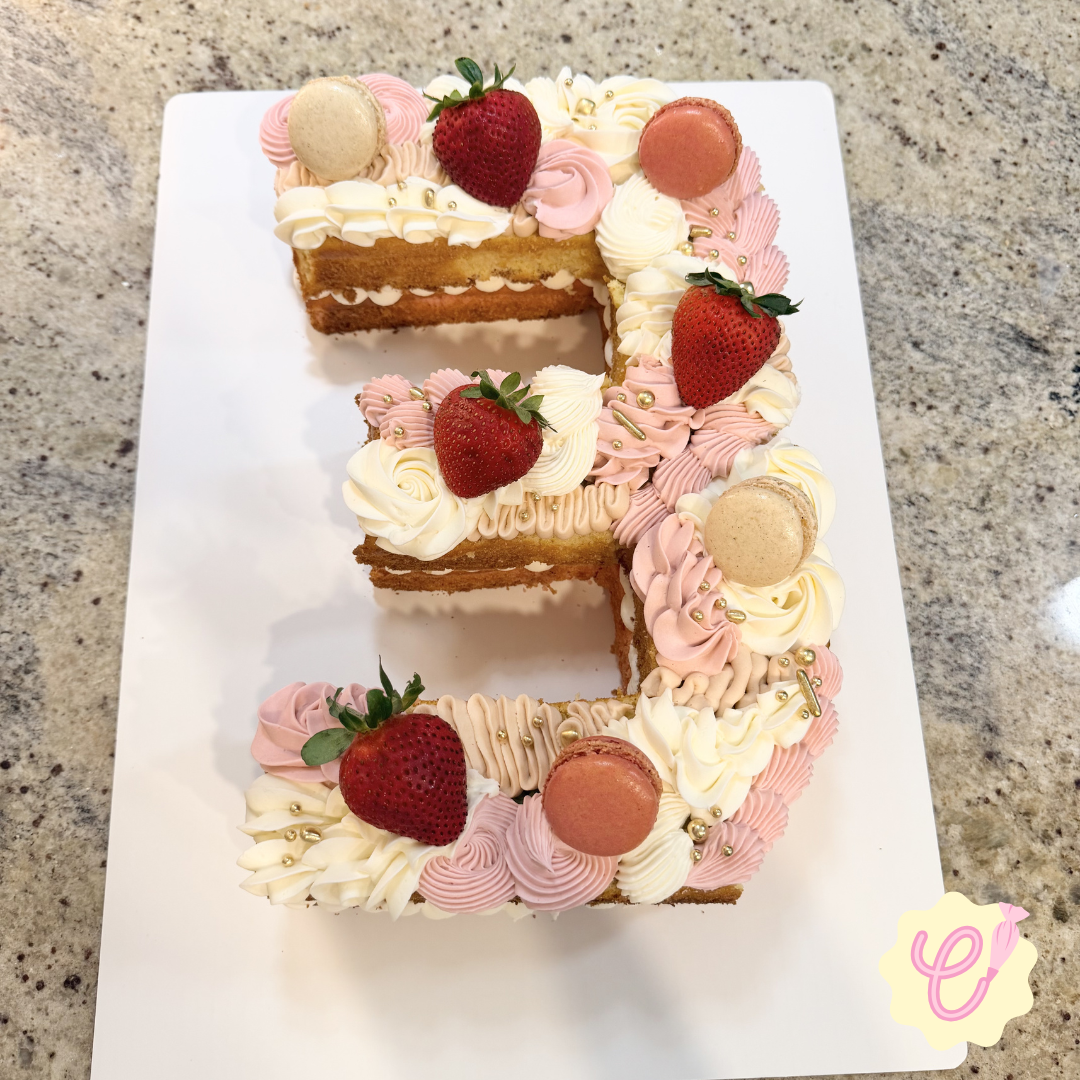 A cake decorated with strawberries, macarons, and pink and white frosting, shaped in the number six.