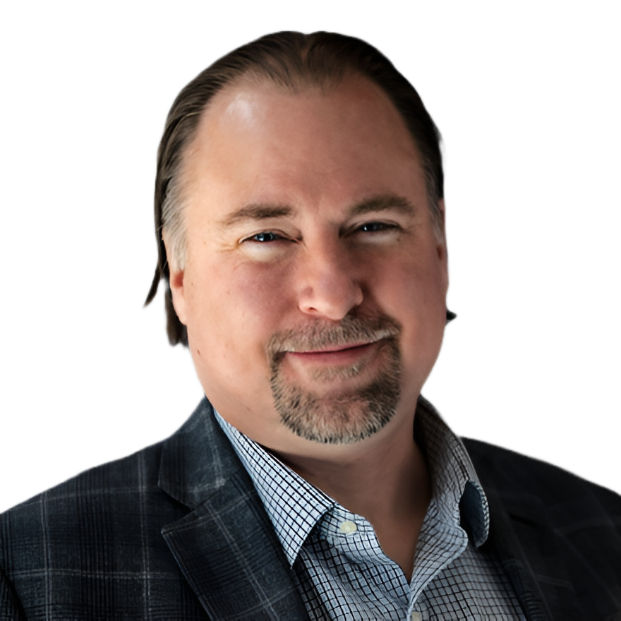 A middle-aged man with dark hair, light skin, and a goatee, wearing a checkered shirt and a dark blazer, smiling at the camera.