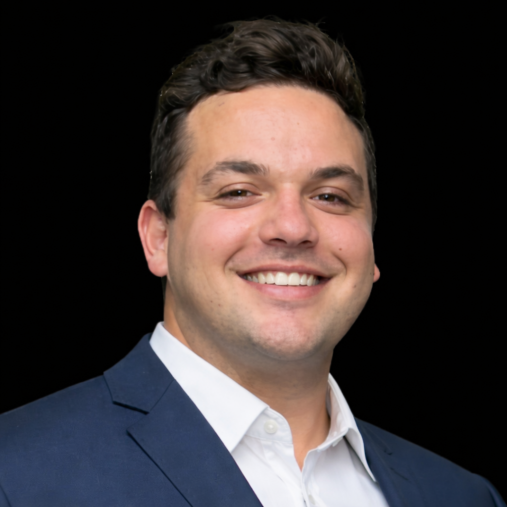 A portrait of a man with short, curly dark hair, wearing a black collared shirt, against a black background.