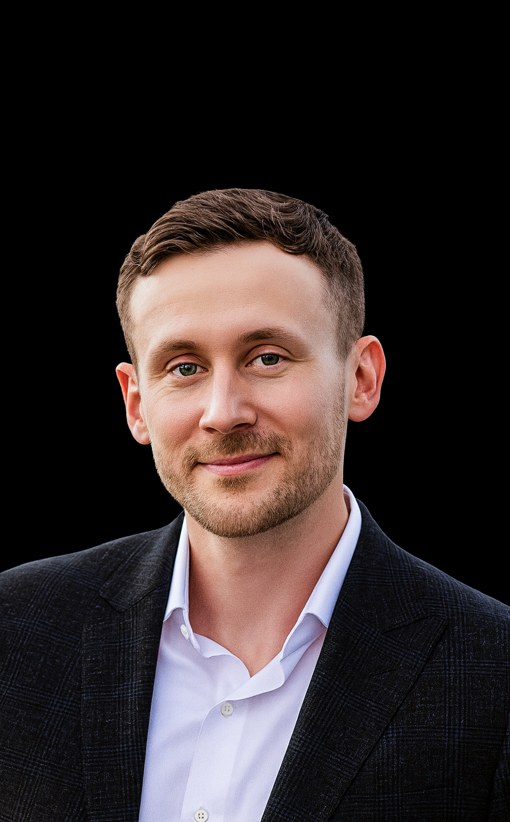 A young man with short brown hair and a beard, wearing a white shirt and a dark blazer, smiling at the camera against a black background.