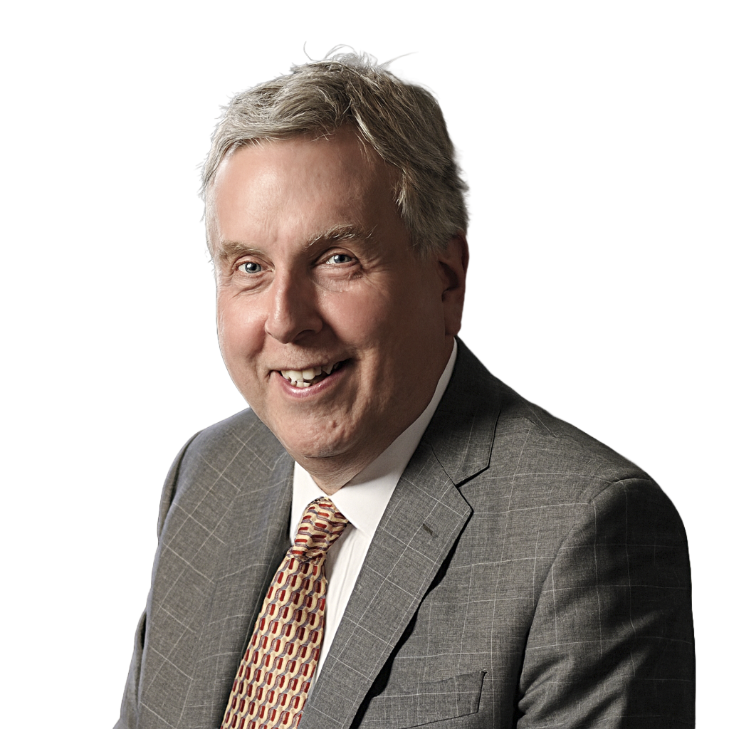 A smiling middle-aged man with gray hair wearing a gray plaid suit, white shirt, and patterned tie.