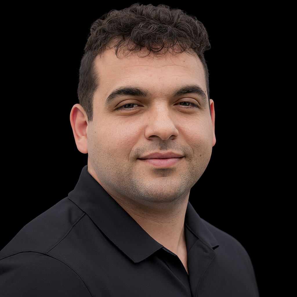 A portrait of a man with short, curly dark hair, wearing a black collared shirt, against a black background.