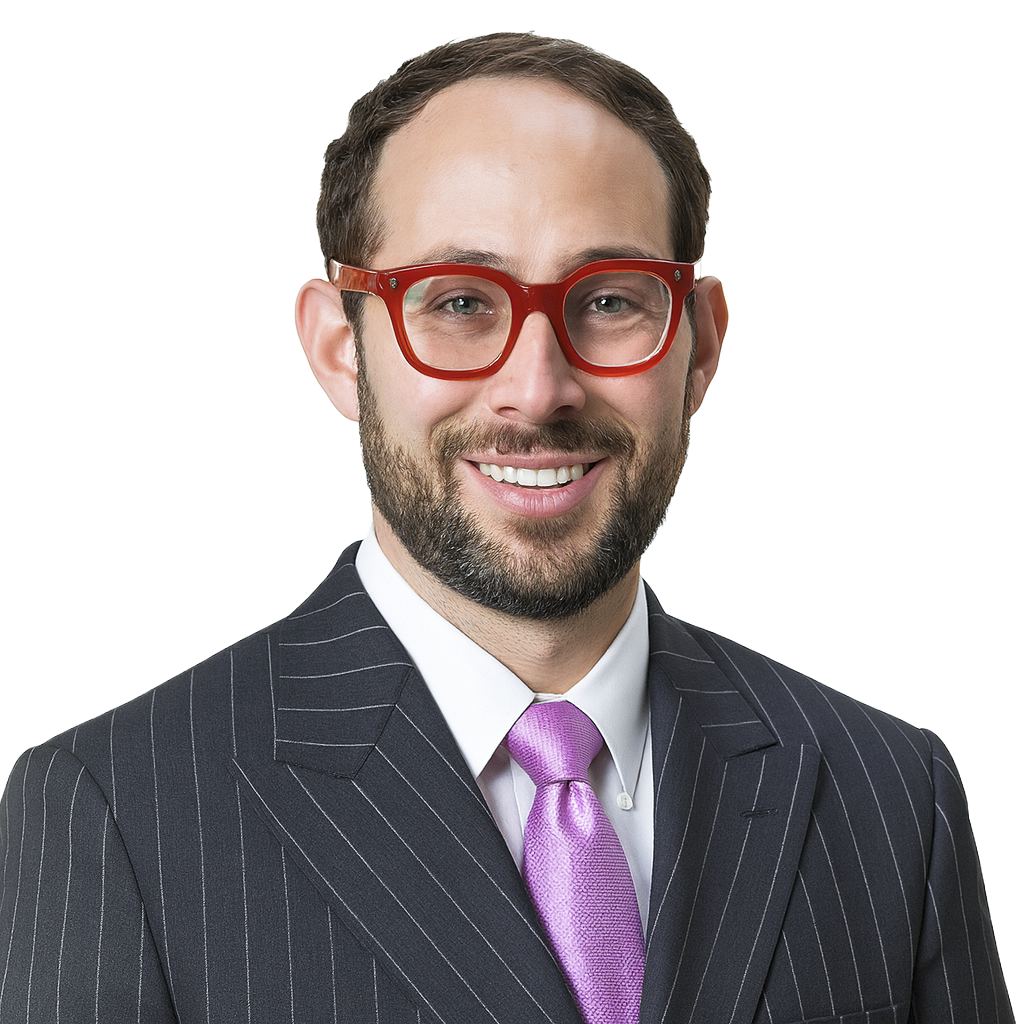 A man with brown hair, a beard, wearing red glasses, a black pinstripe suit, white shirt, and a purple tie, smiling at the camera.
