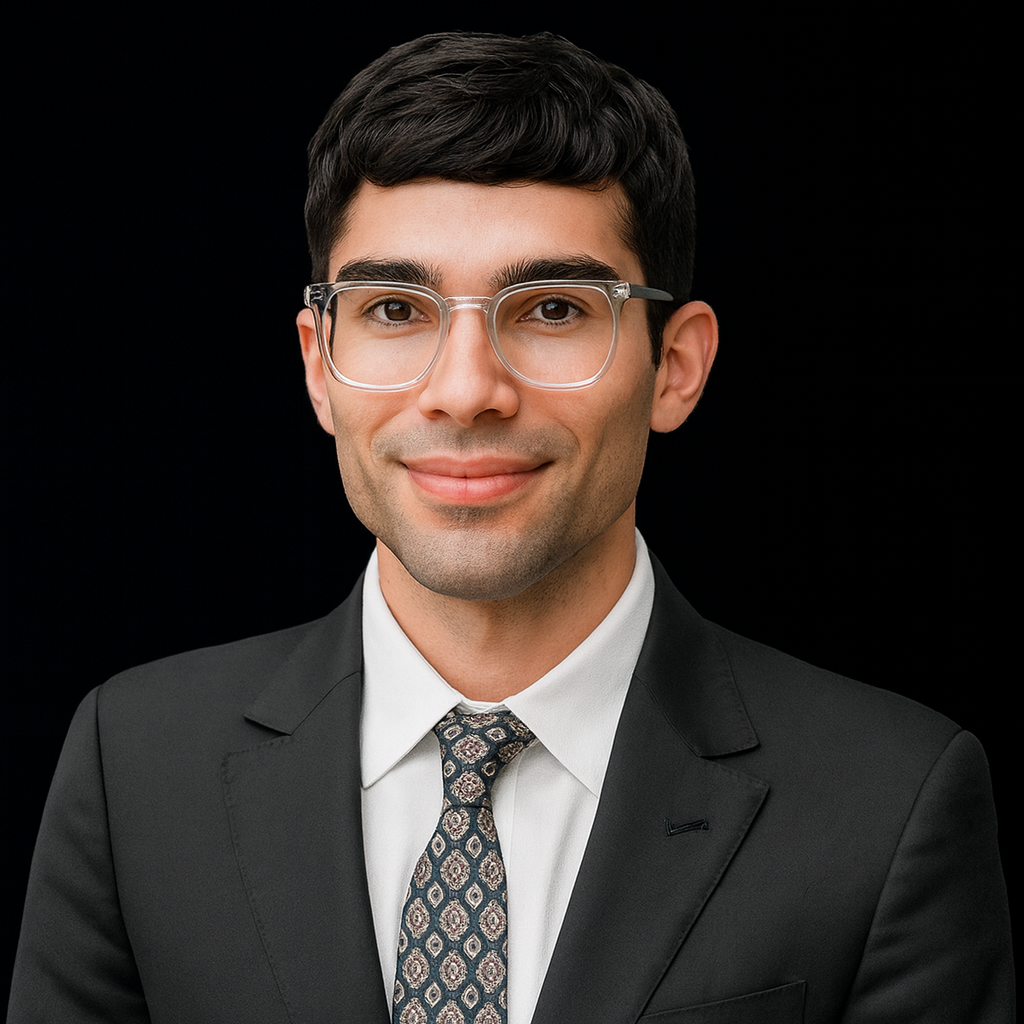 A young man with dark hair, wearing glasses, a white shirt, a patterned tie, and a black suit jacket, smiling against a black background.