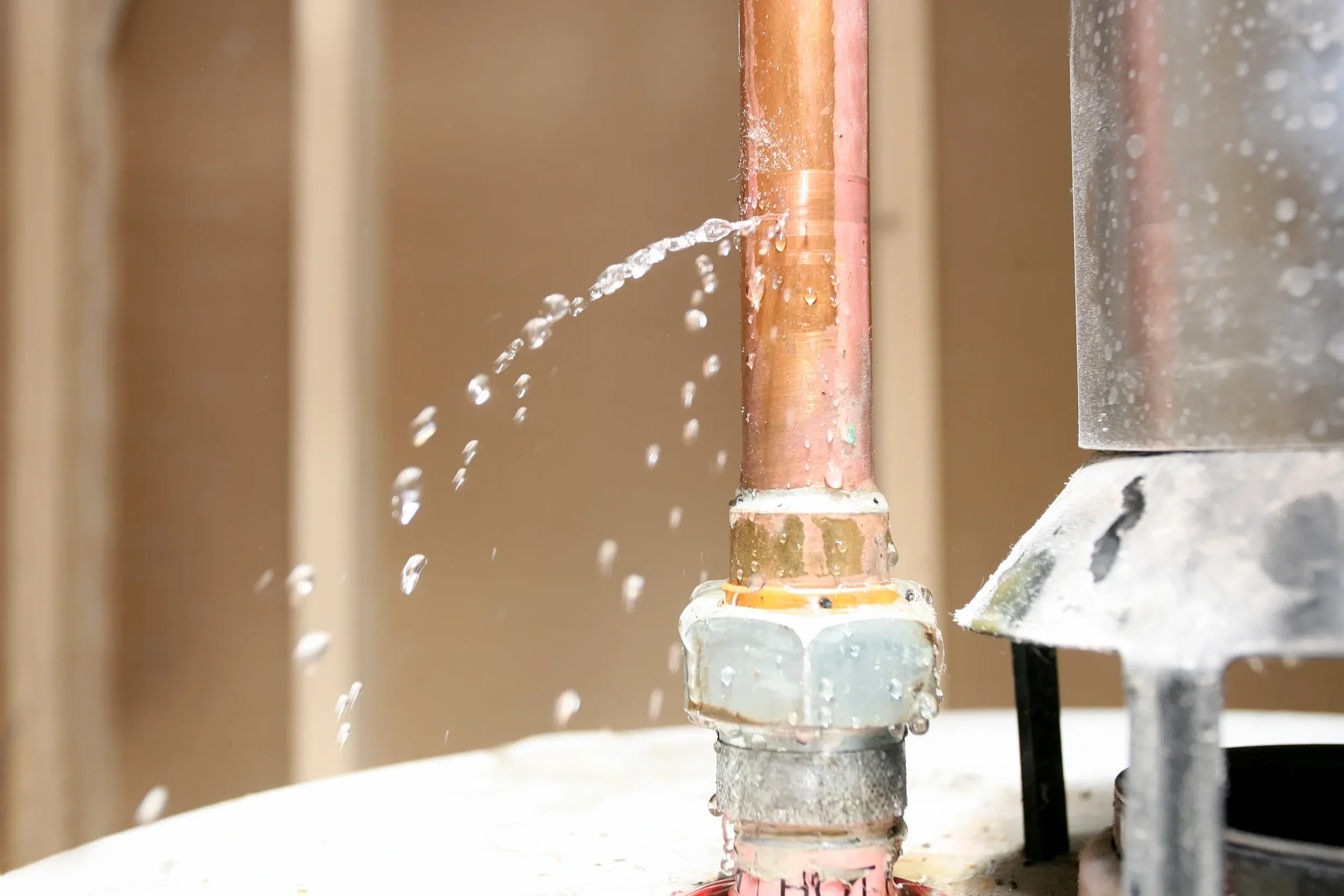 Close-up of a copper and metal pipe with water leaking from the joint. Water droplets are splashing and dripping from the pipe.