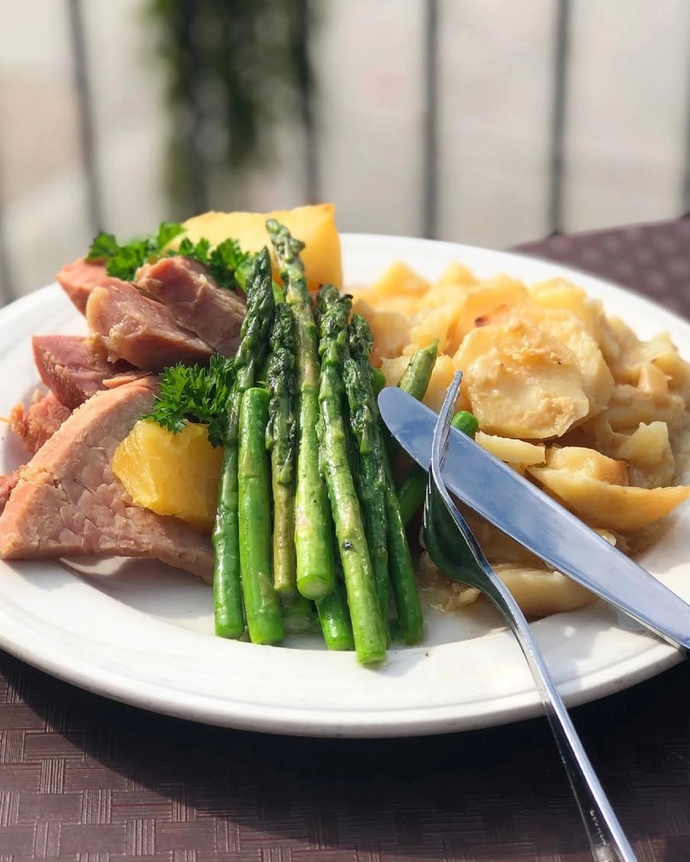 Plate of cooked asparagus, mashed potatoes with gravy, roast chicken, and some greens on a white plate.