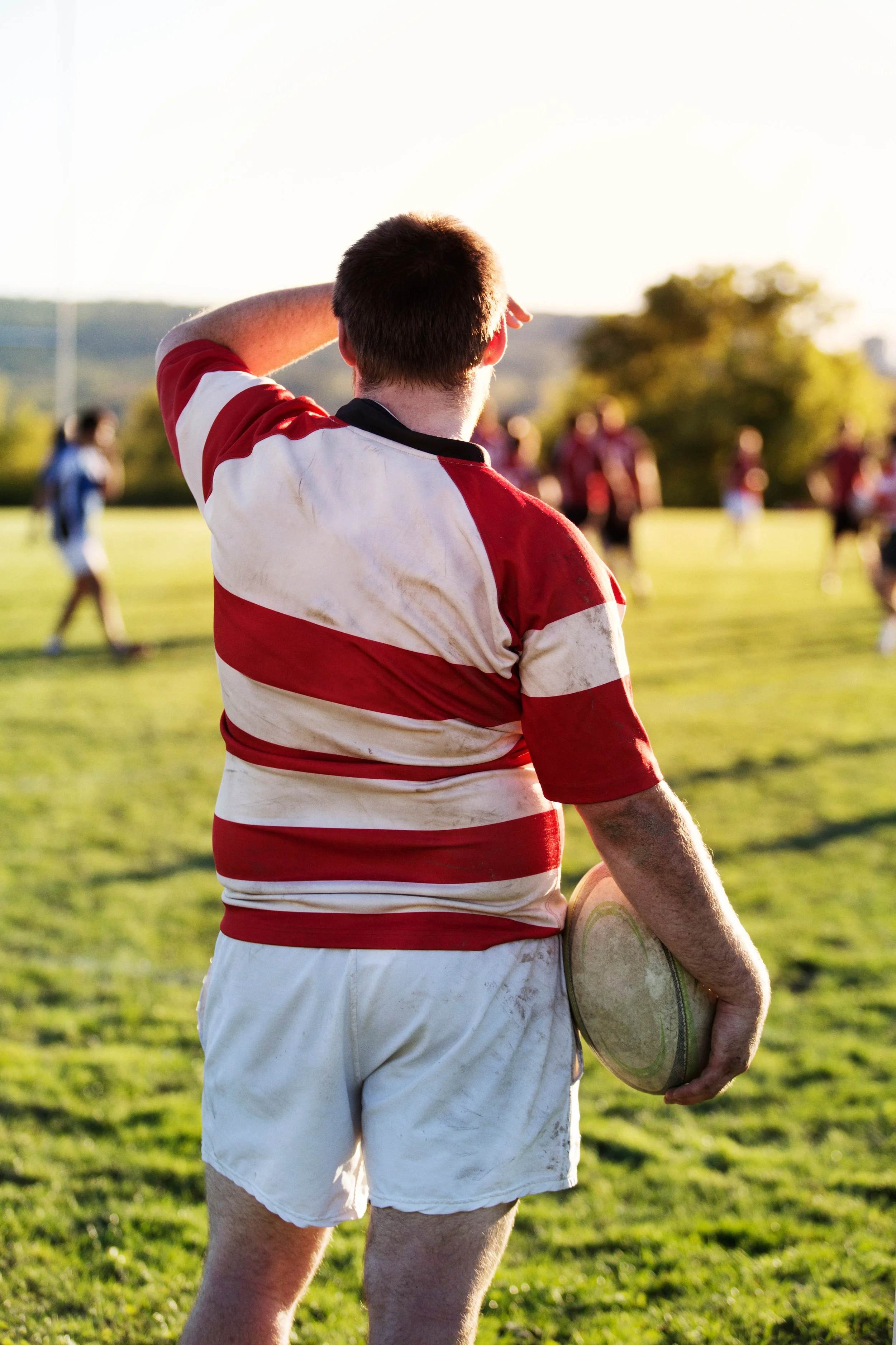 Rugby player in red and white striped jersey holding rugby ball on field.