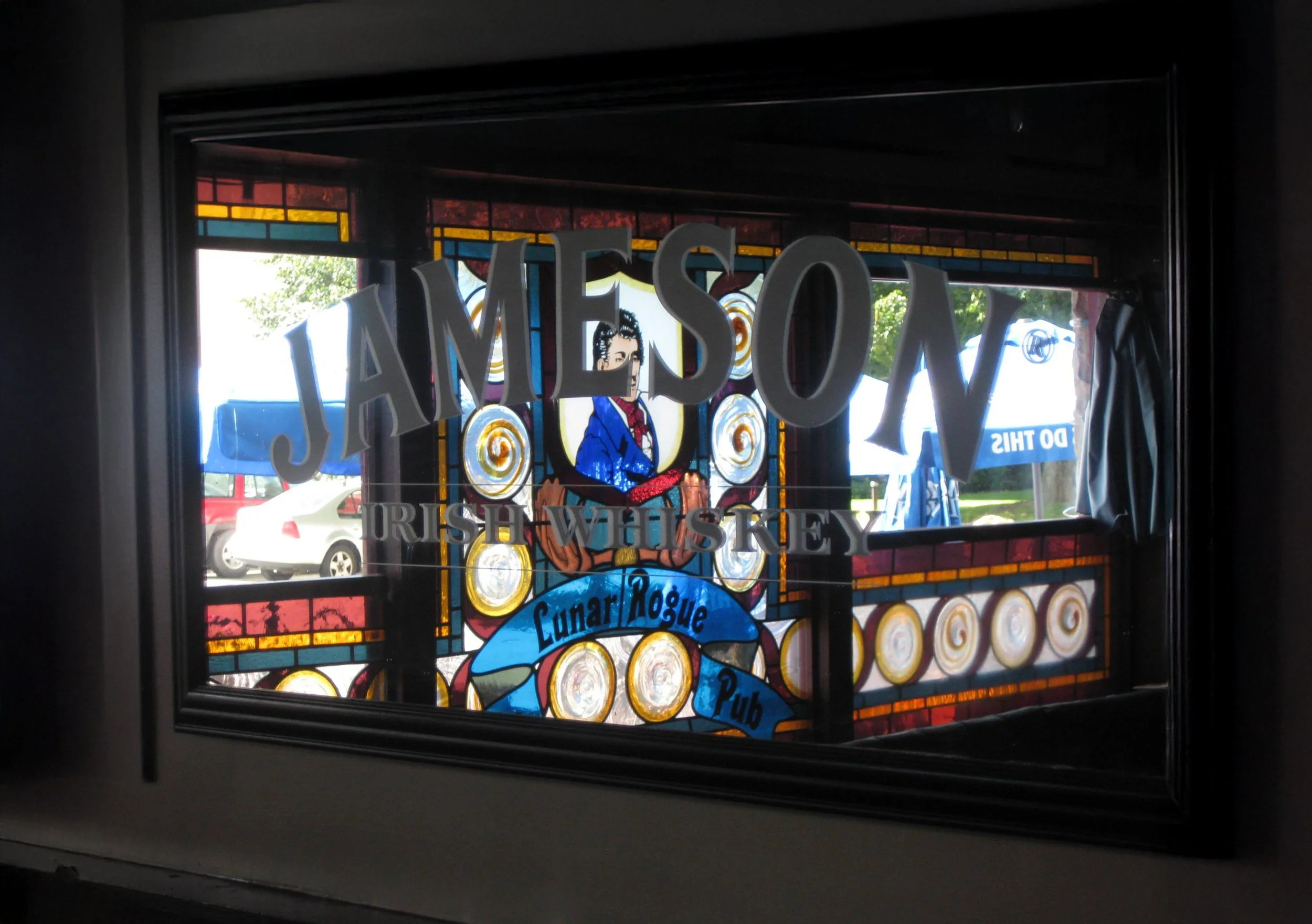 Decorative stained glass window featuring a woman in historical attire with the words "JAMESON Irish Whiskey" and "Lunar Rogue Pub".