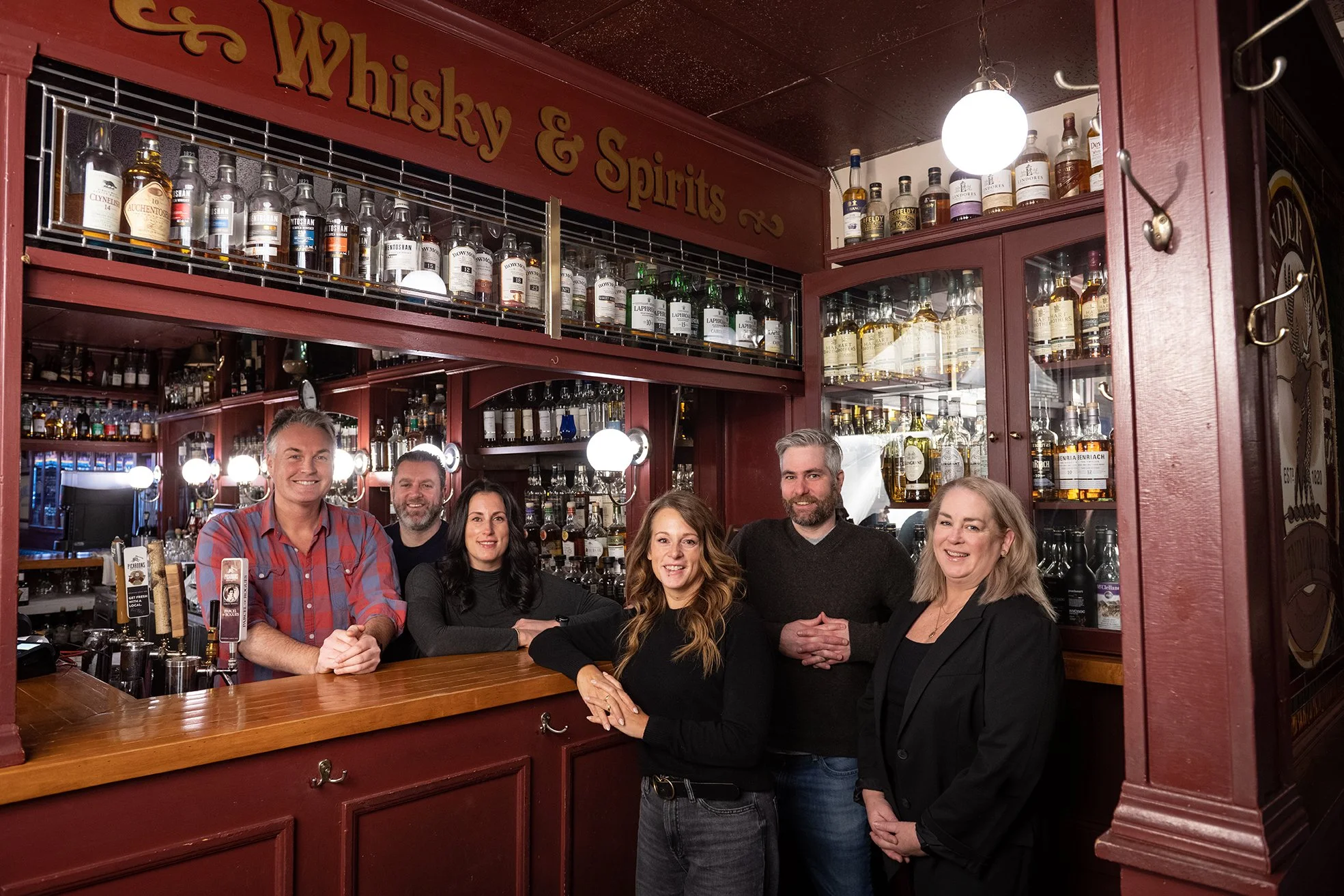 Group of six people smiling inside a whiskey and spirits bar.
