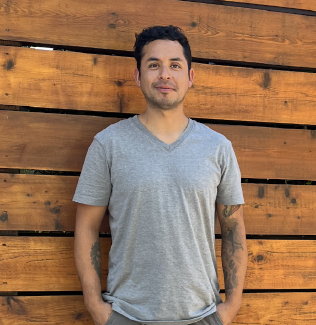 Man standing in front of a wooden fence, wearing a gray t-shirt and smiling.