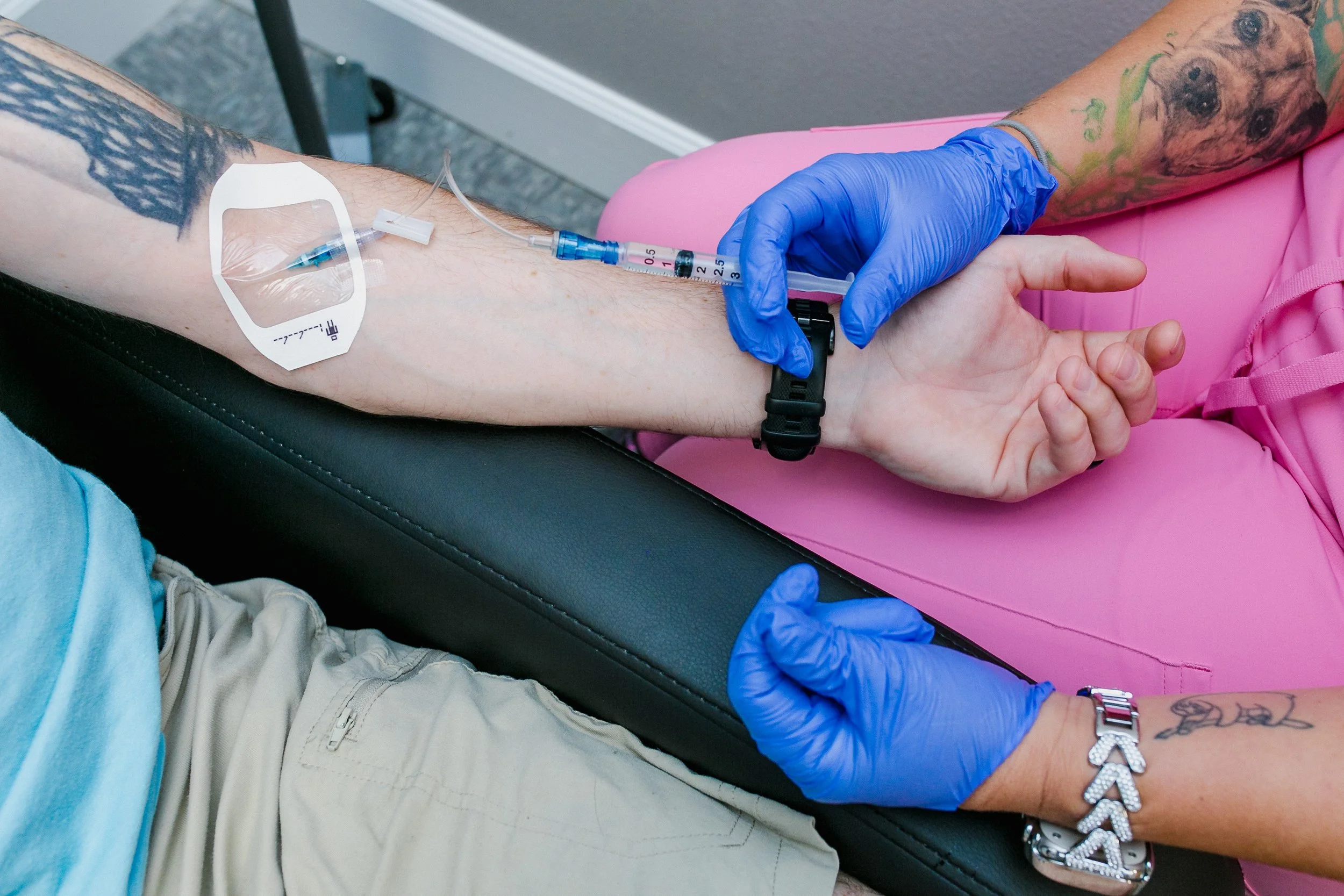 A person getting an IV bag while a healthcare worker in blue gloves holds their arm.