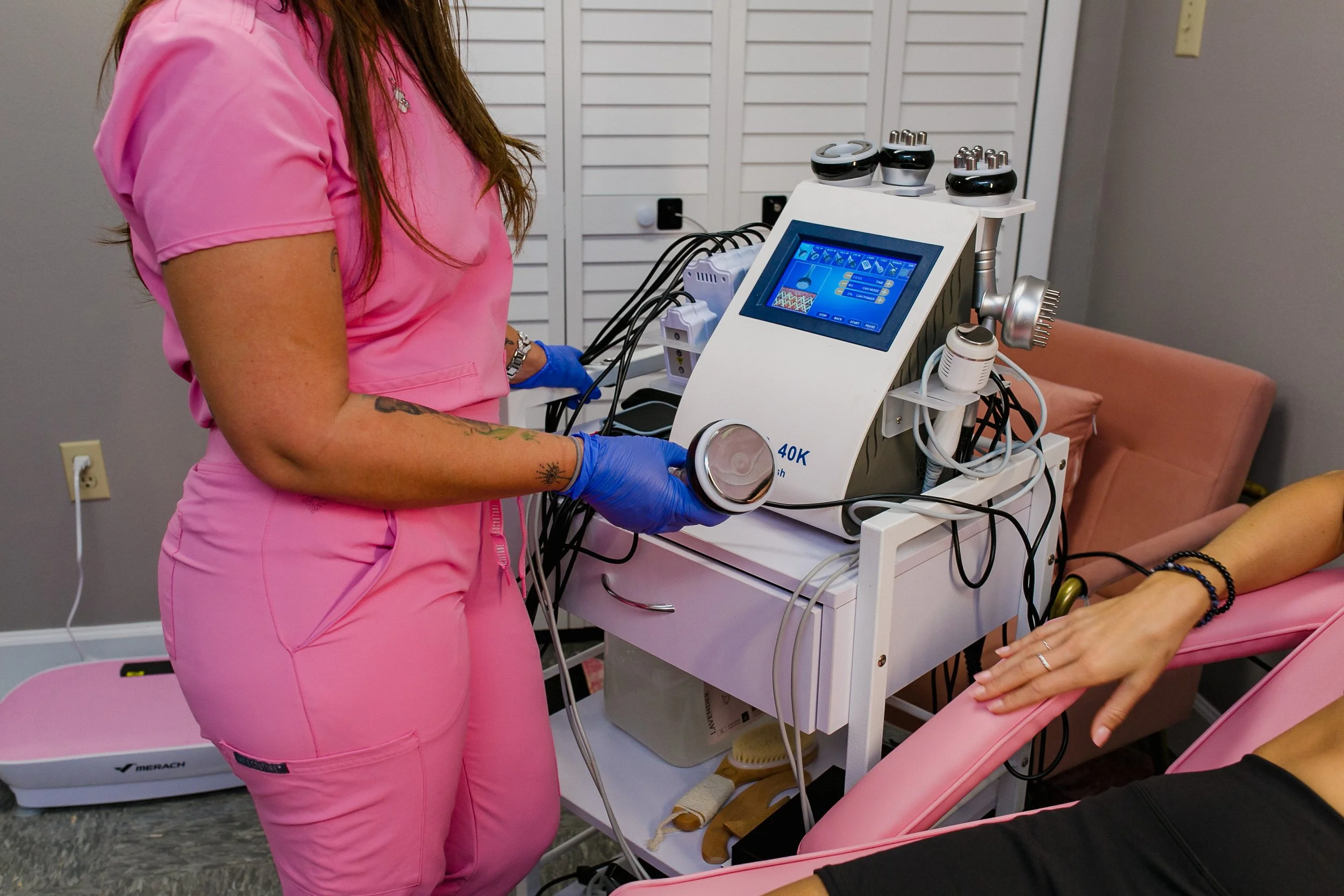 Medical professional in pink scrubs and blue gloves operating a medical device during a treatment session with a patient in a medical clinic.
