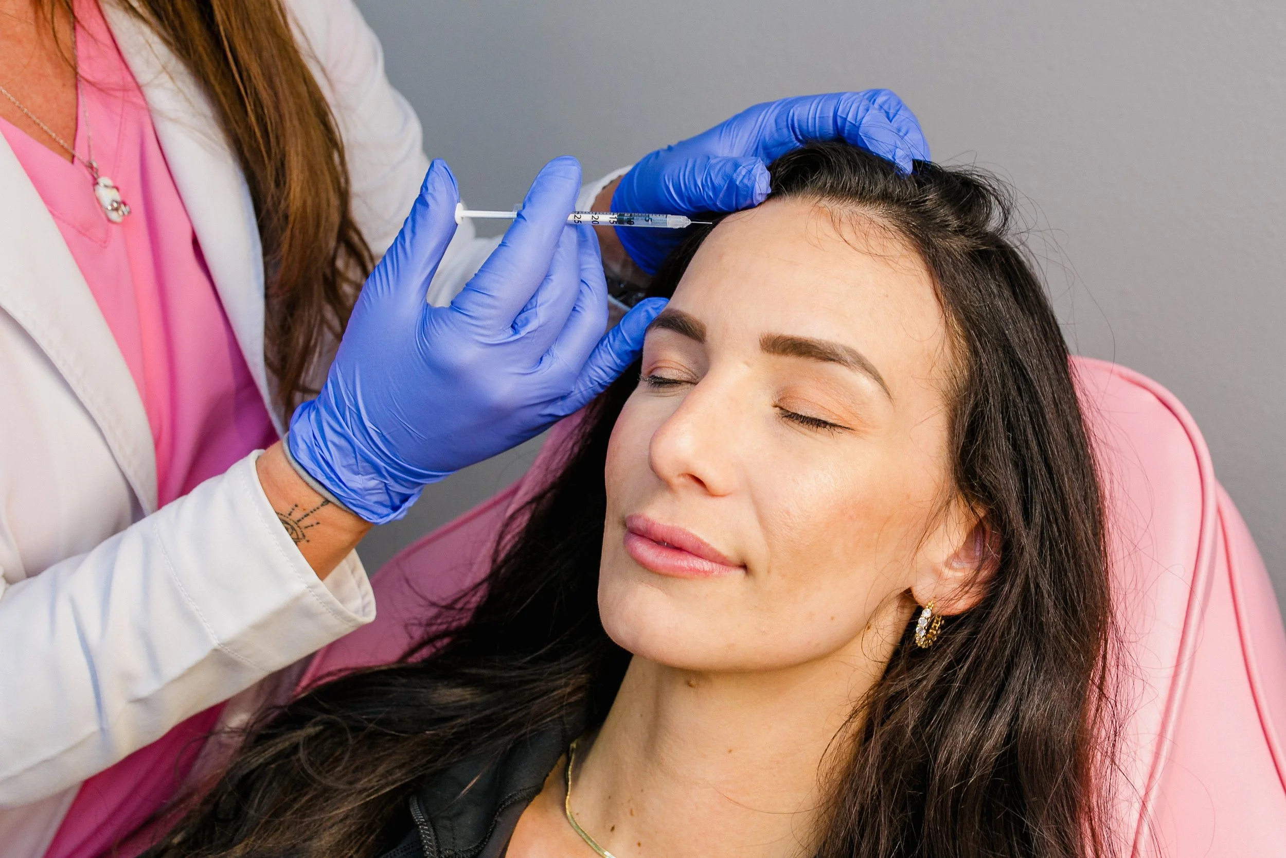 A woman receiving a Botox injection in her forehead from a healthcare professional wearing blue gloves.