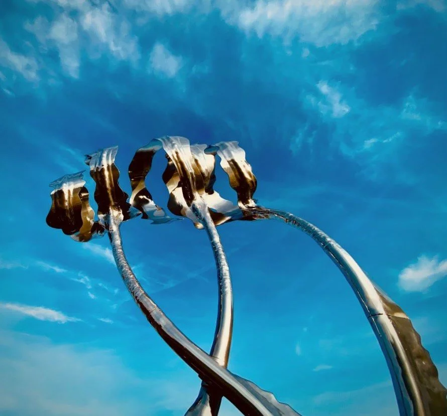 Close-up of metallic kelp sculpture against a blue sky with scattered clouds.