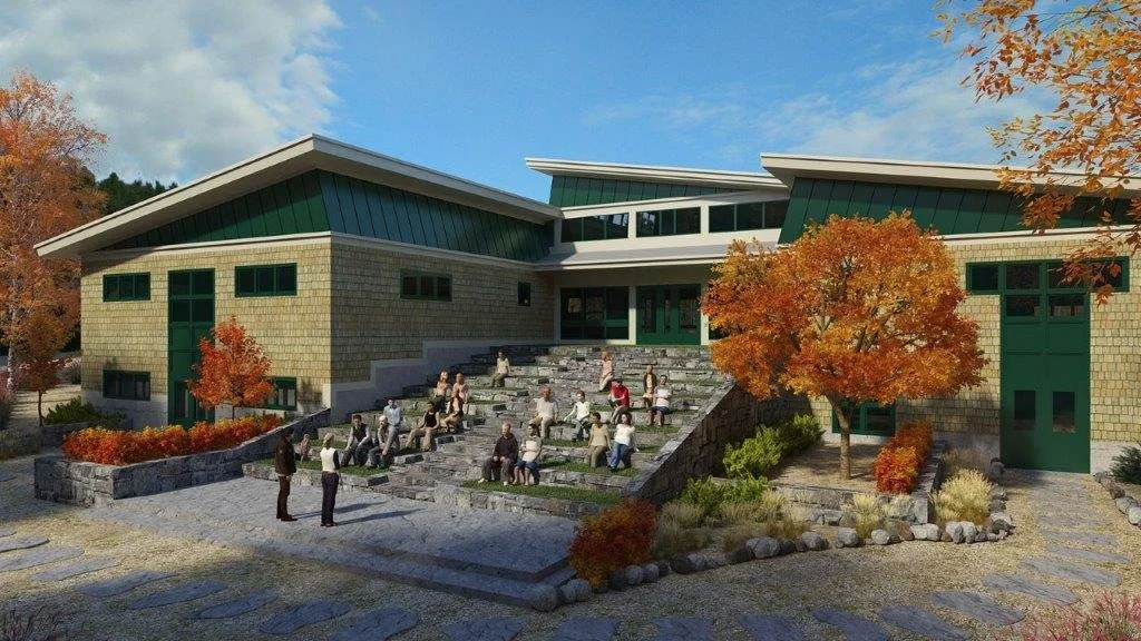 A modern building with green accents and a sloped roof, featuring an outdoor seating area with steps and people sitting and socializing.