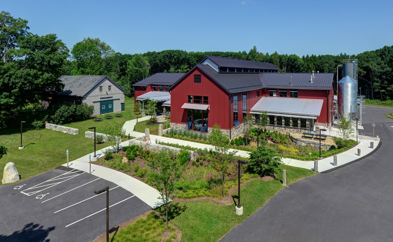 A modern red and gray building surrounded by landscaped gardens, trees, and parking lot with designated handicapped parking spaces, in a rural setting with a blue sky overhead.