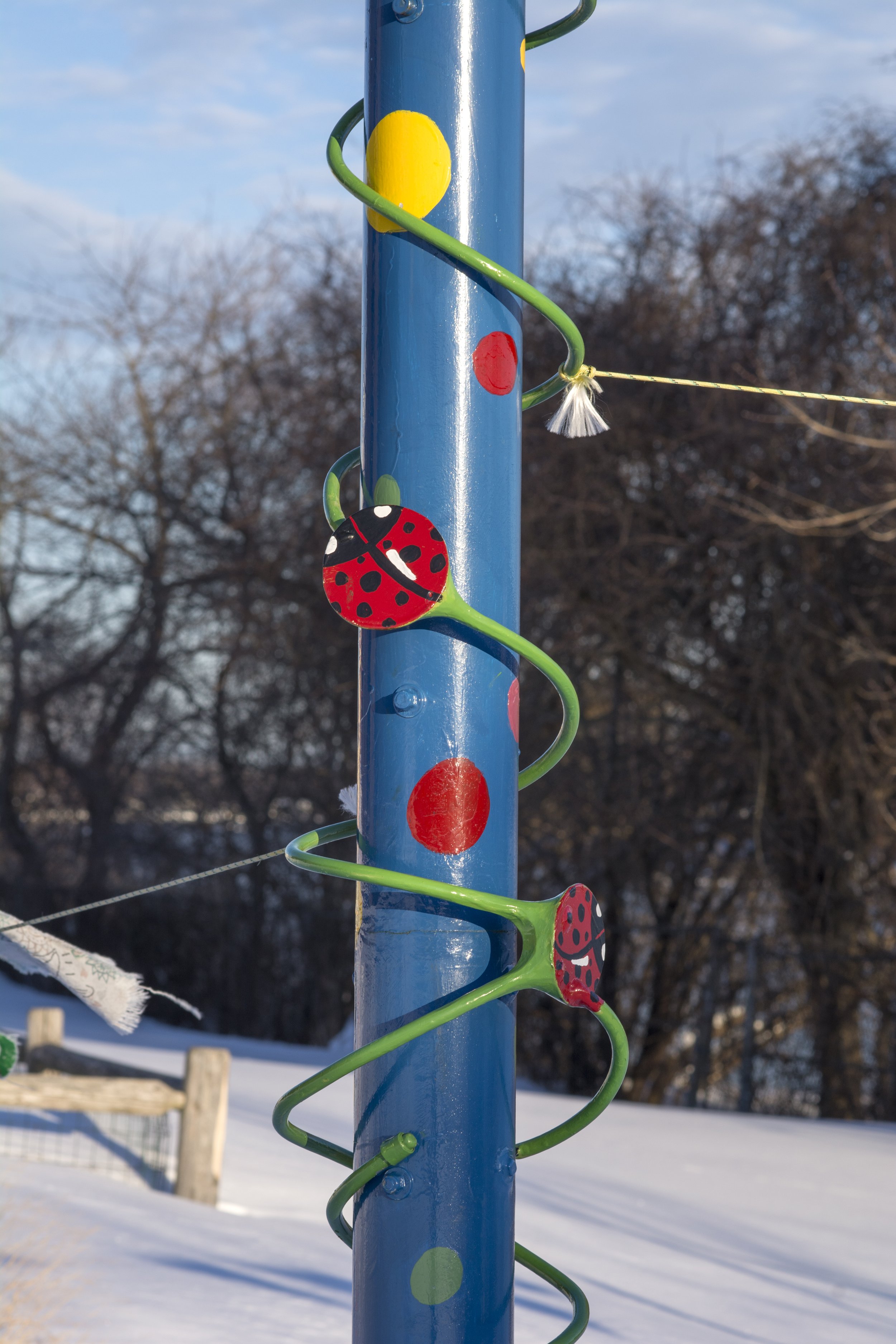Colorful pole decorated with ladybug and polka dot designs against a snowy outdoor background.