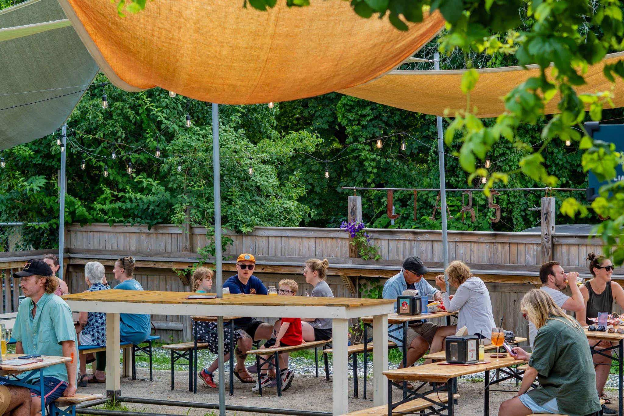 People sitting and dining outdoors at a backyard patio with string lights and shade sails.