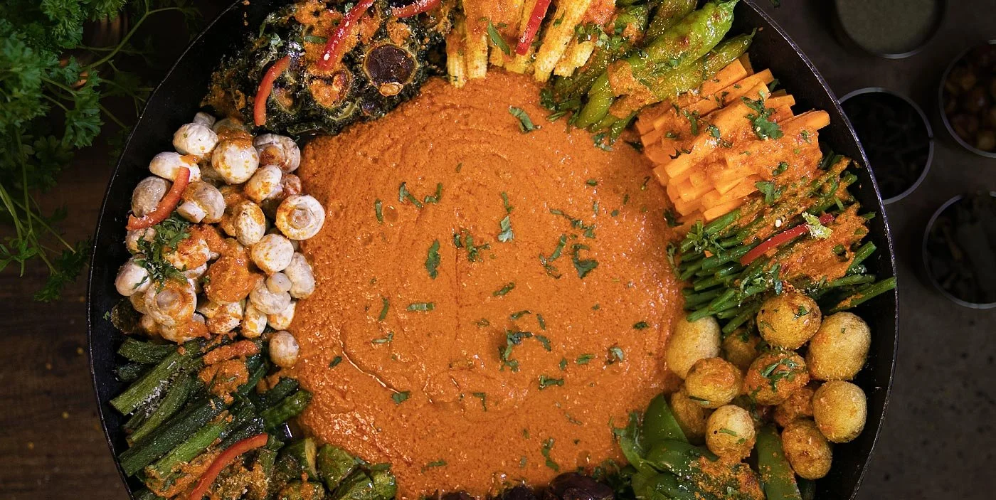 A large platter of Indian vegetarian dishes including chickpea curry, vegetable stew, assorted vegetables with spices, and a variety of cooked vegetables garnished with herbs.