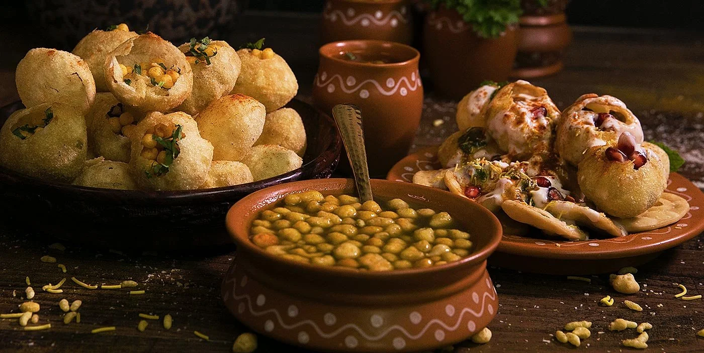Traditional Mexican food spread with fried arancini-filled with chickpeas, topped with herbs, accompanied by yellow chickpeas in a terracotta bowl, and a plate of filled fried bread rolls with sauce, garnished with herbs and pomegranate seeds, set on