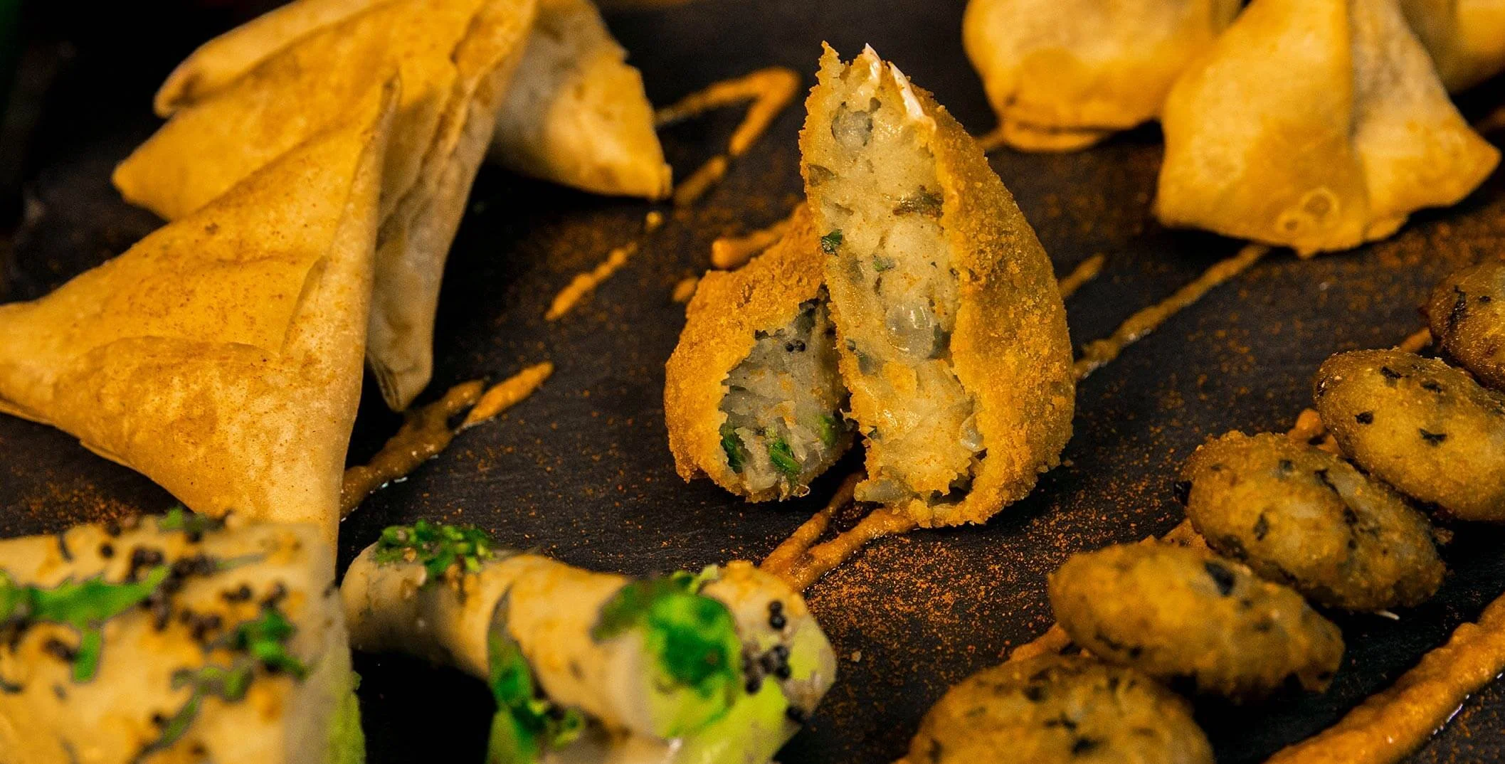 Close-up of assorted Asian appetizers including fried dumplings, egg rolls, and skewered snacks on a dark platter.