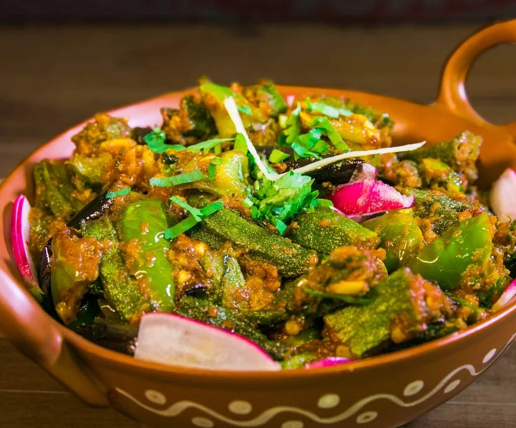 A bowl of Indian vegetable curry garnished with chopped green herbs and slices of radish.