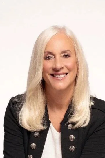 A smiling woman with blonde hair against a dark background.