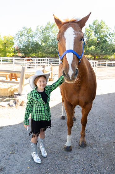Children grooming a brown horse in a stable.