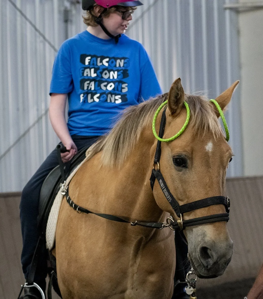 A young person participates in an adaptive riding lesson at The Right Step, Inc. The horse has neon green rings on its ears.
