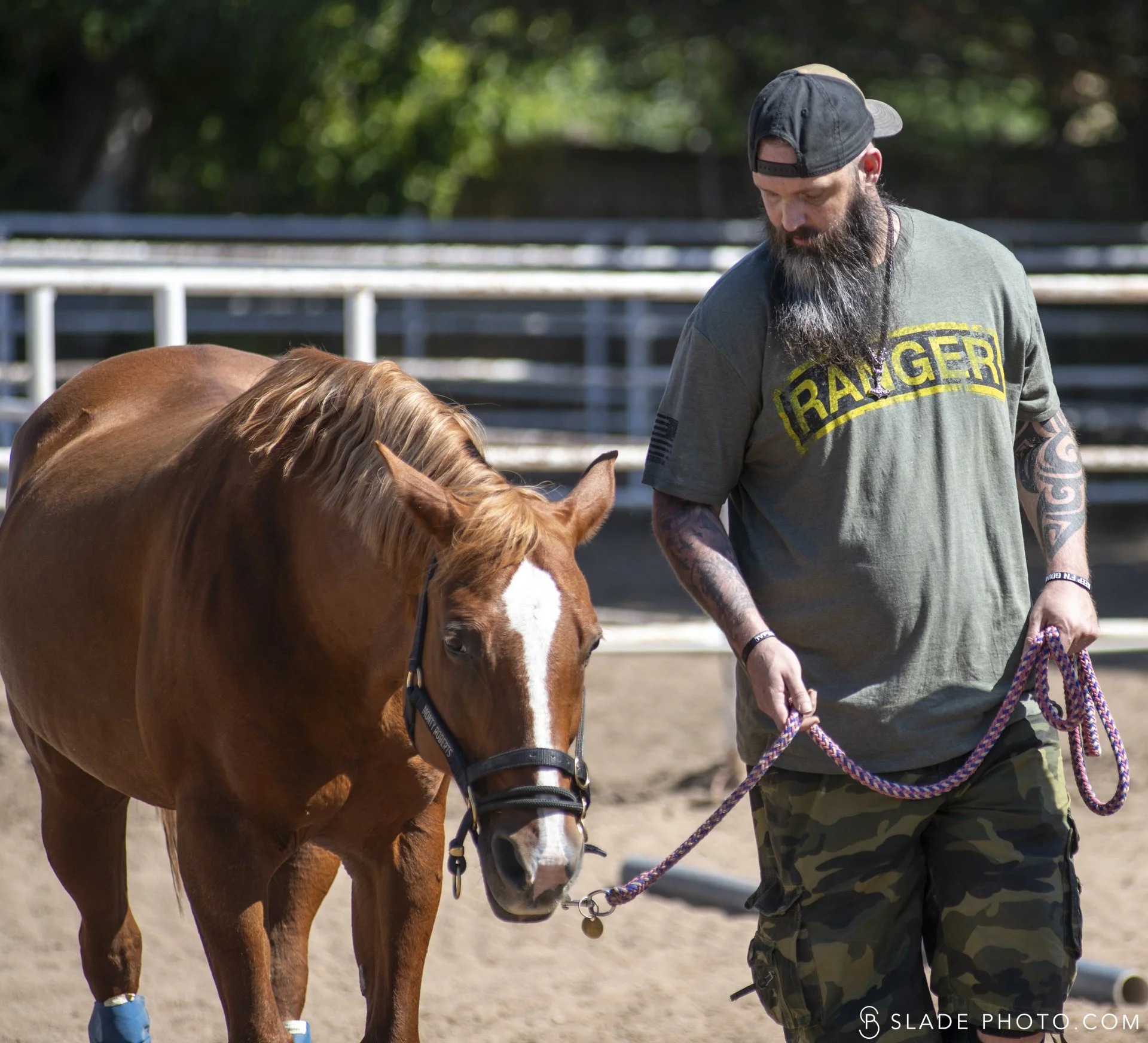 A veteran participating in The Right Step Inc. ground program, standing next to a chestnut horse on a dirt field with trees in the background.