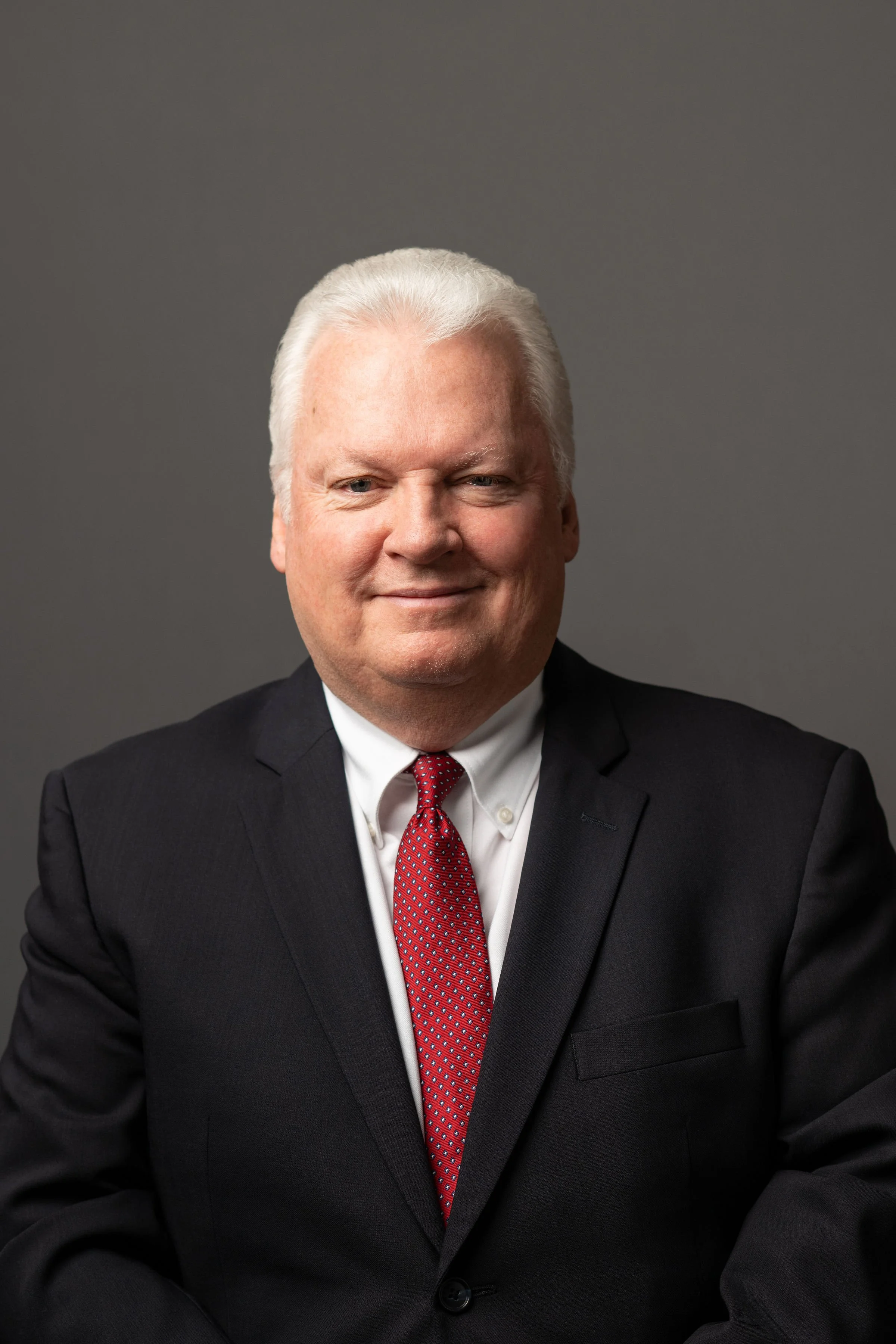 Headshot of Doug Morton wearing a suit in front of gray background