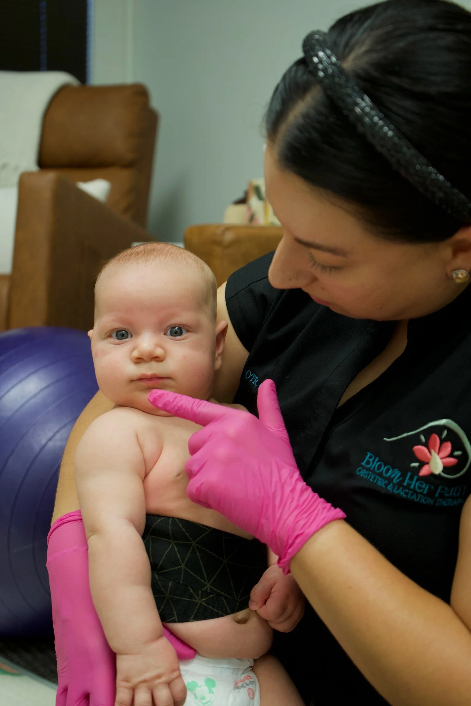 Haydee Medrano, co-owner of Bloom Her Path and occupational therapist, holds infant on lap and has pink gloves on to work on oral ties, pre and post-frenectomy care, and improve sucking, swallowing, and coordination