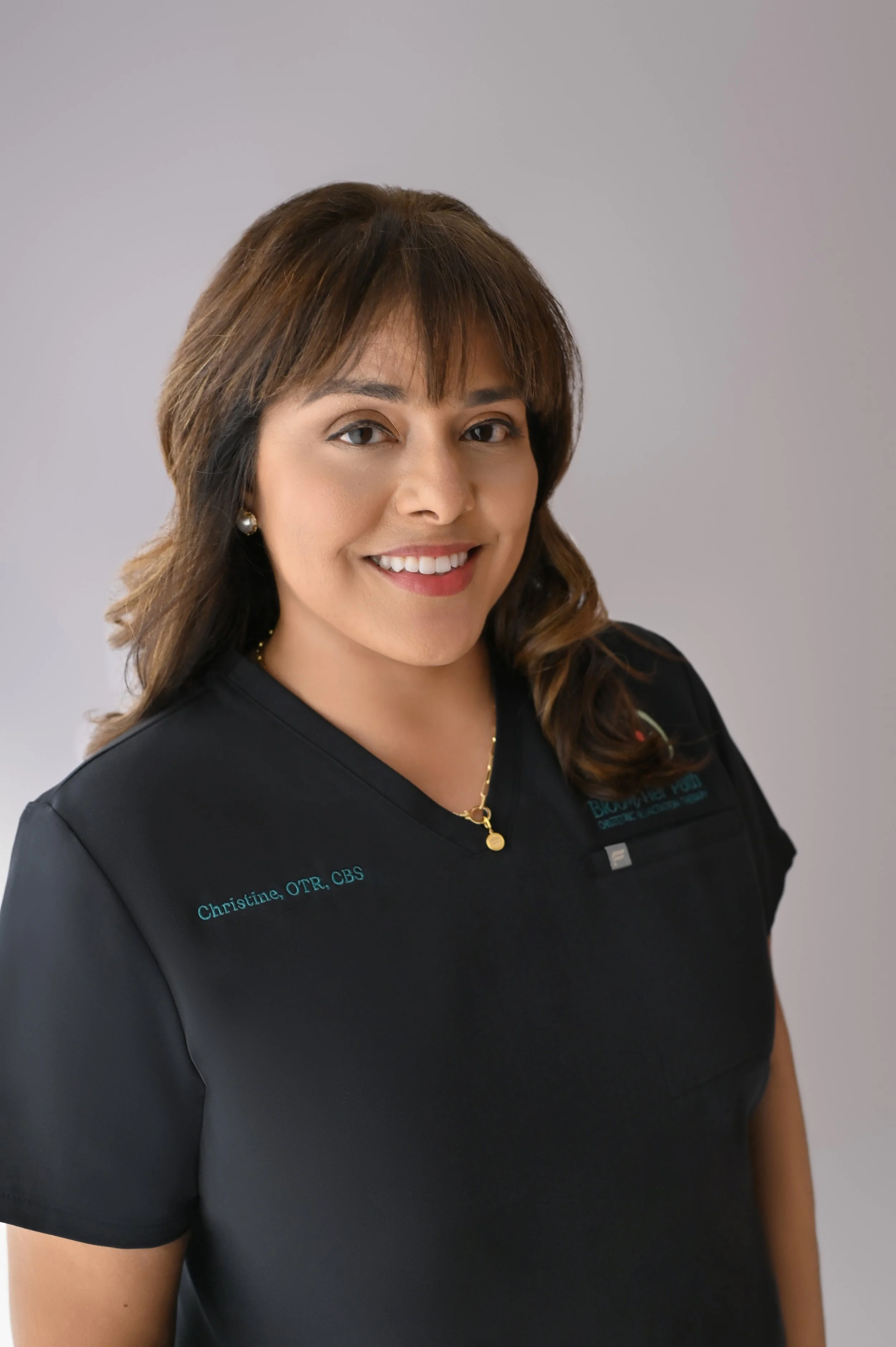 Christine Hernandez headshot with her dark hair down and black scrubs on. She is a co-owner of Bloom Her Path in Corpus Christi, TX