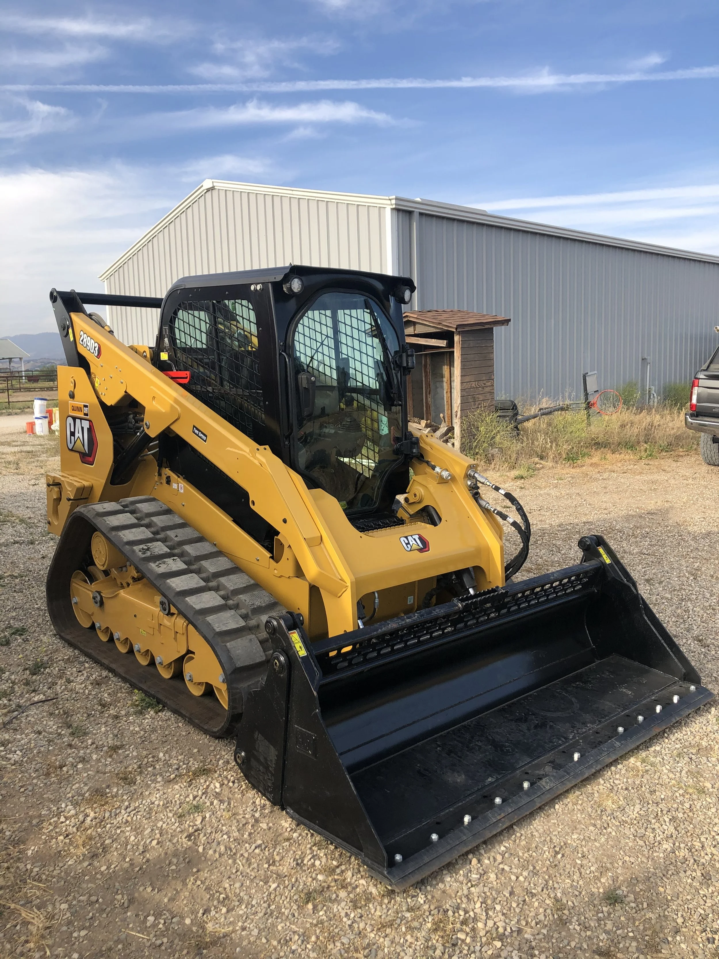 A red water truck with a large silver tank driving on a dirt road with trees in the background.