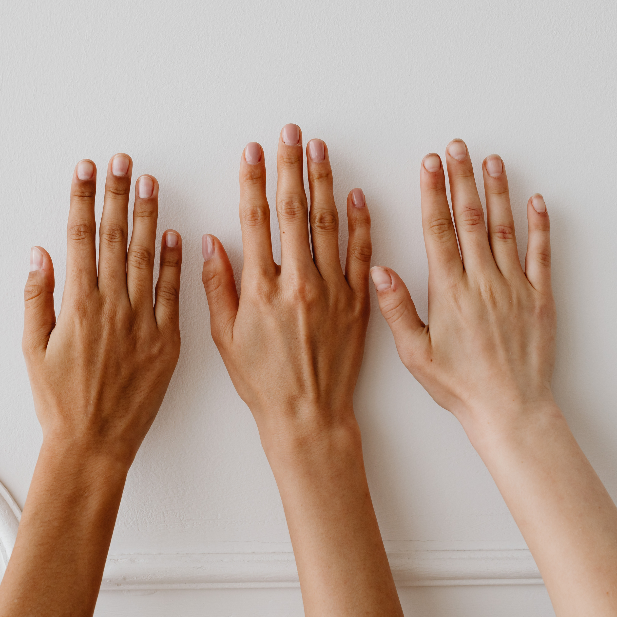 Three hands with different skin tones placed on a white wall.