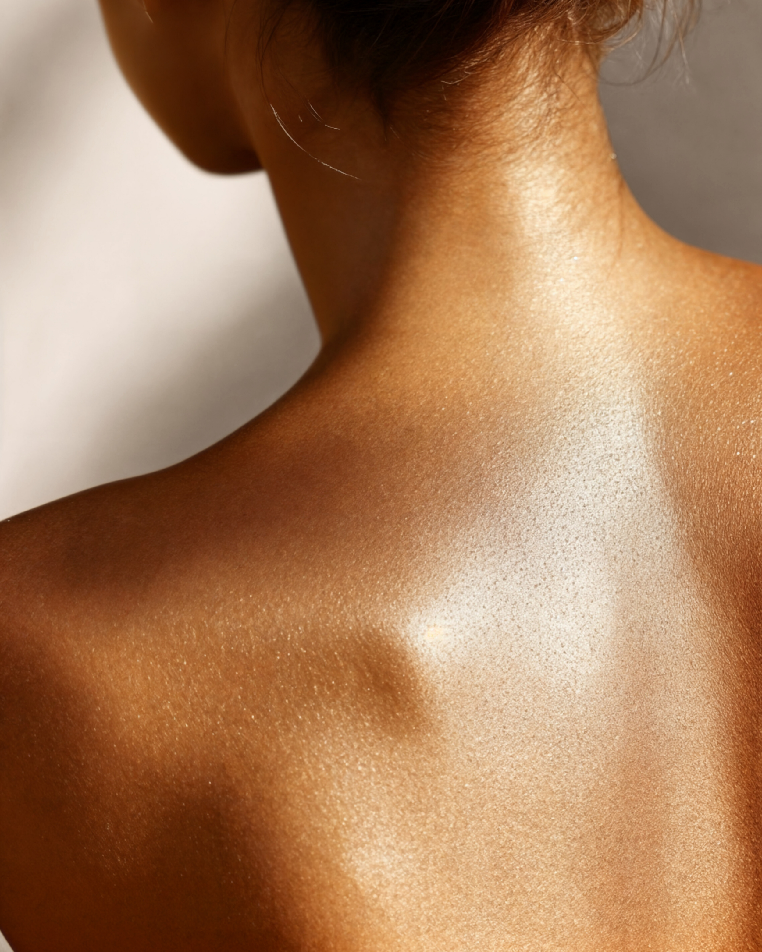 Close-up of a woman's neck and shoulder, showcasing smooth, glowing, tan skin with a subtle shimmer.