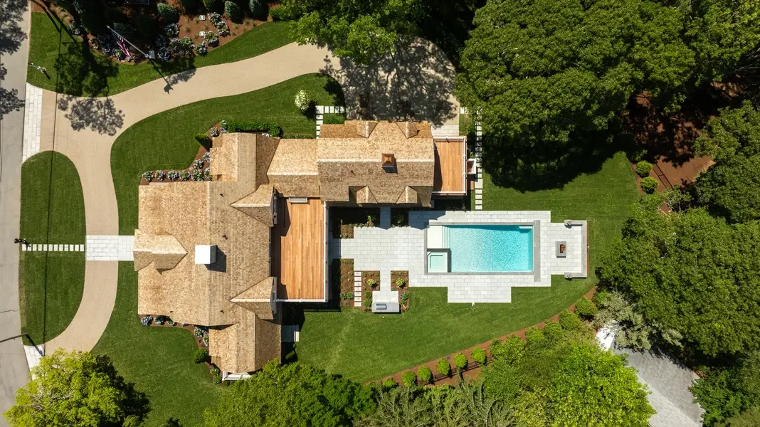 Overhead drone shot of elegant estate property with custom pool, spa, outdoor living spaces, professional landscaping, and private wooded setting